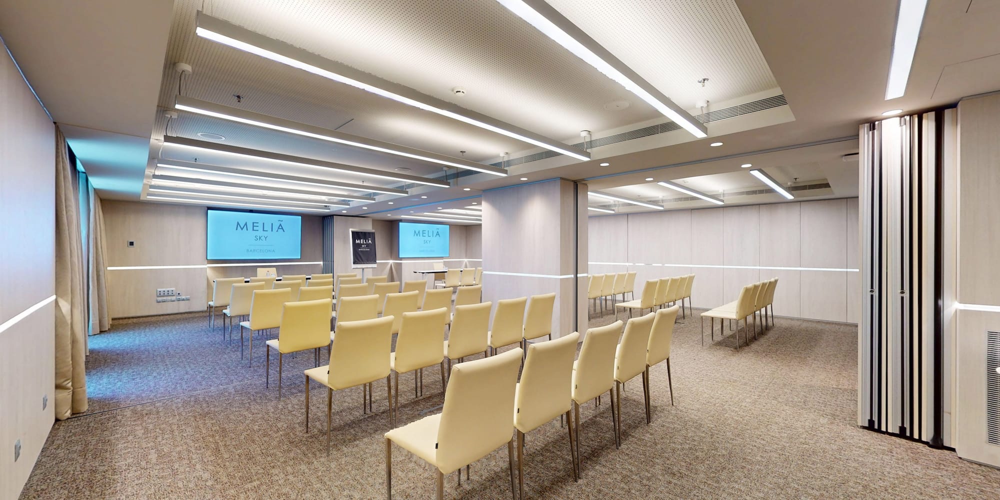 Meliá Sky modern meeting room with screen, rows of chairs, and light wood design.