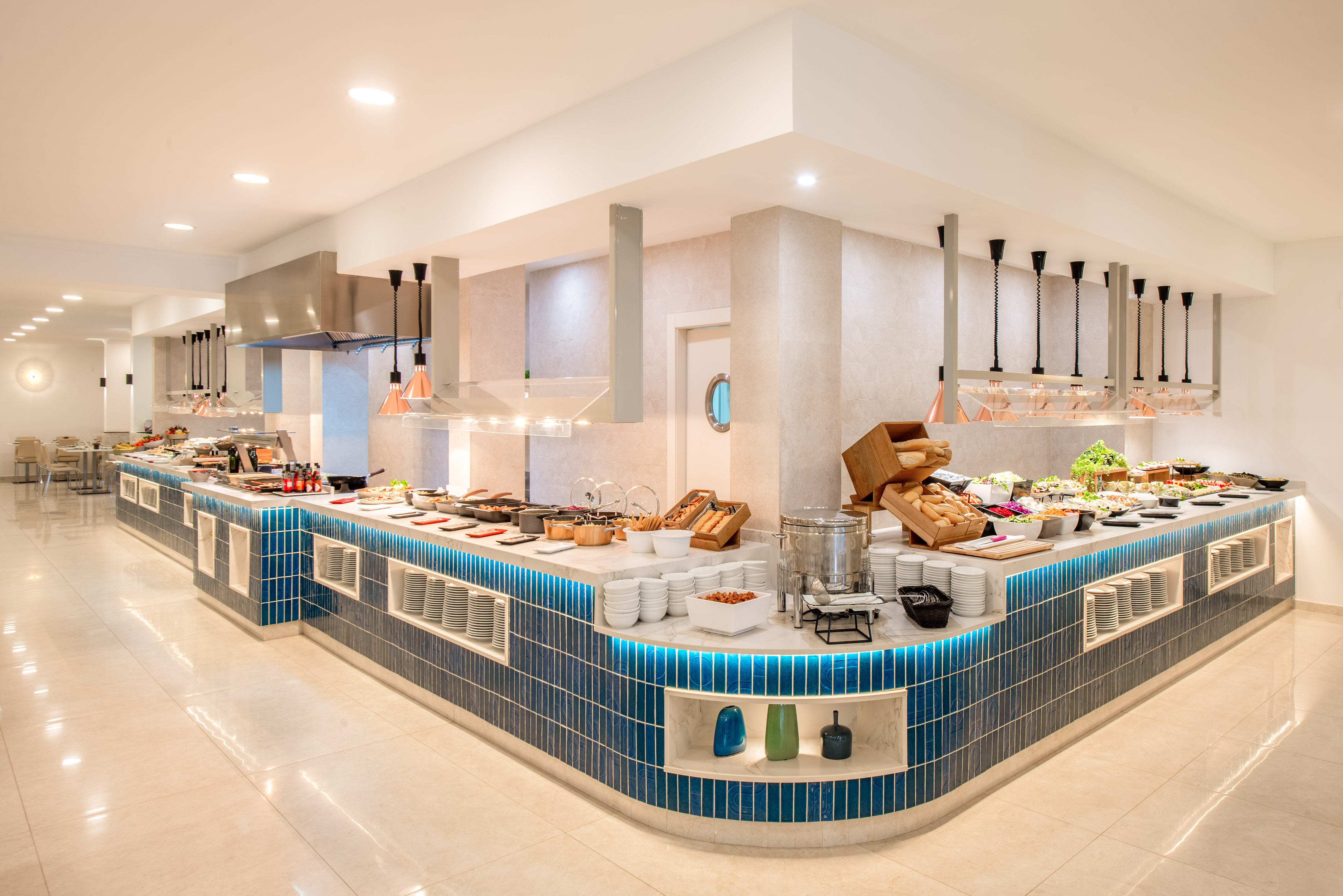 Spacious hotel buffet with varied food, blue tiled counter, and modern design.