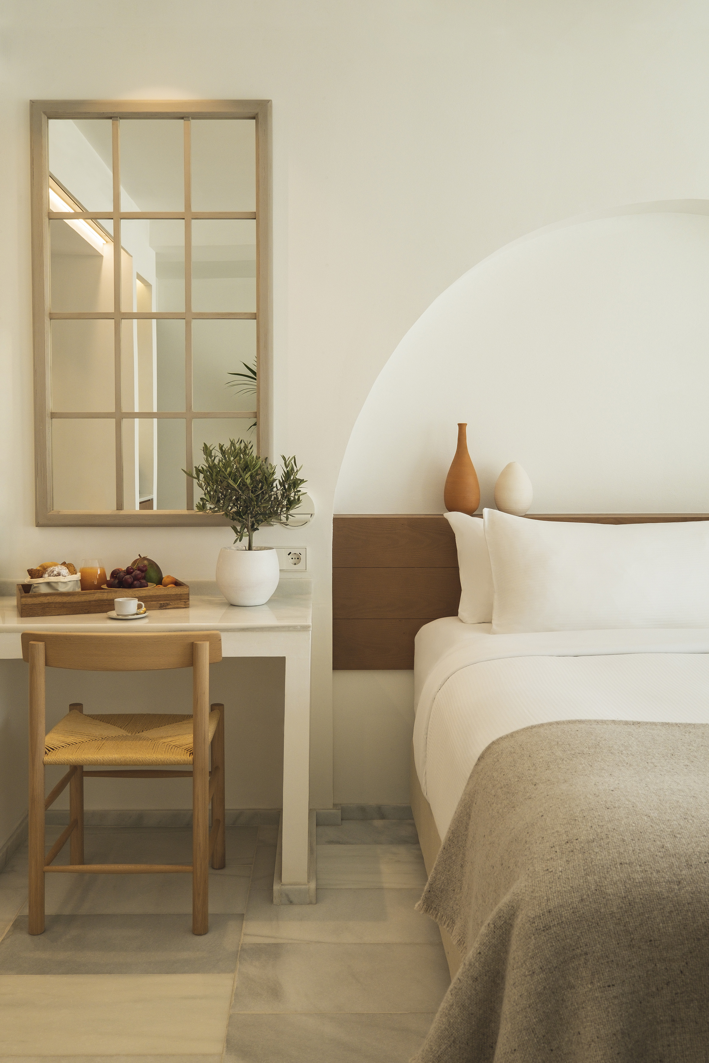 Modern minimalist hotel room with white bed, desk, mirror, and breakfast.