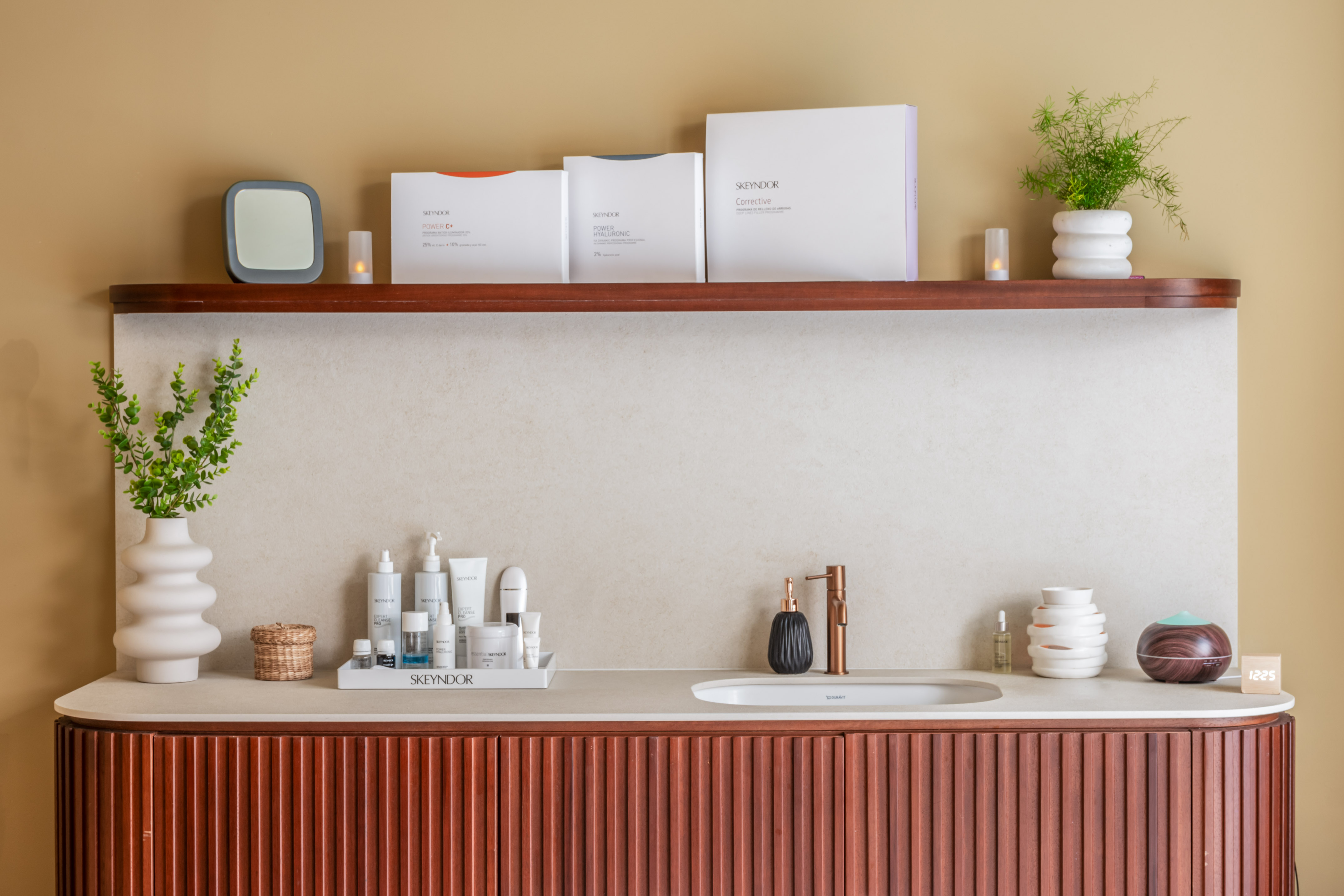 Elegant Skeyndor skincare vanity with fluted wood cabinet and plants.