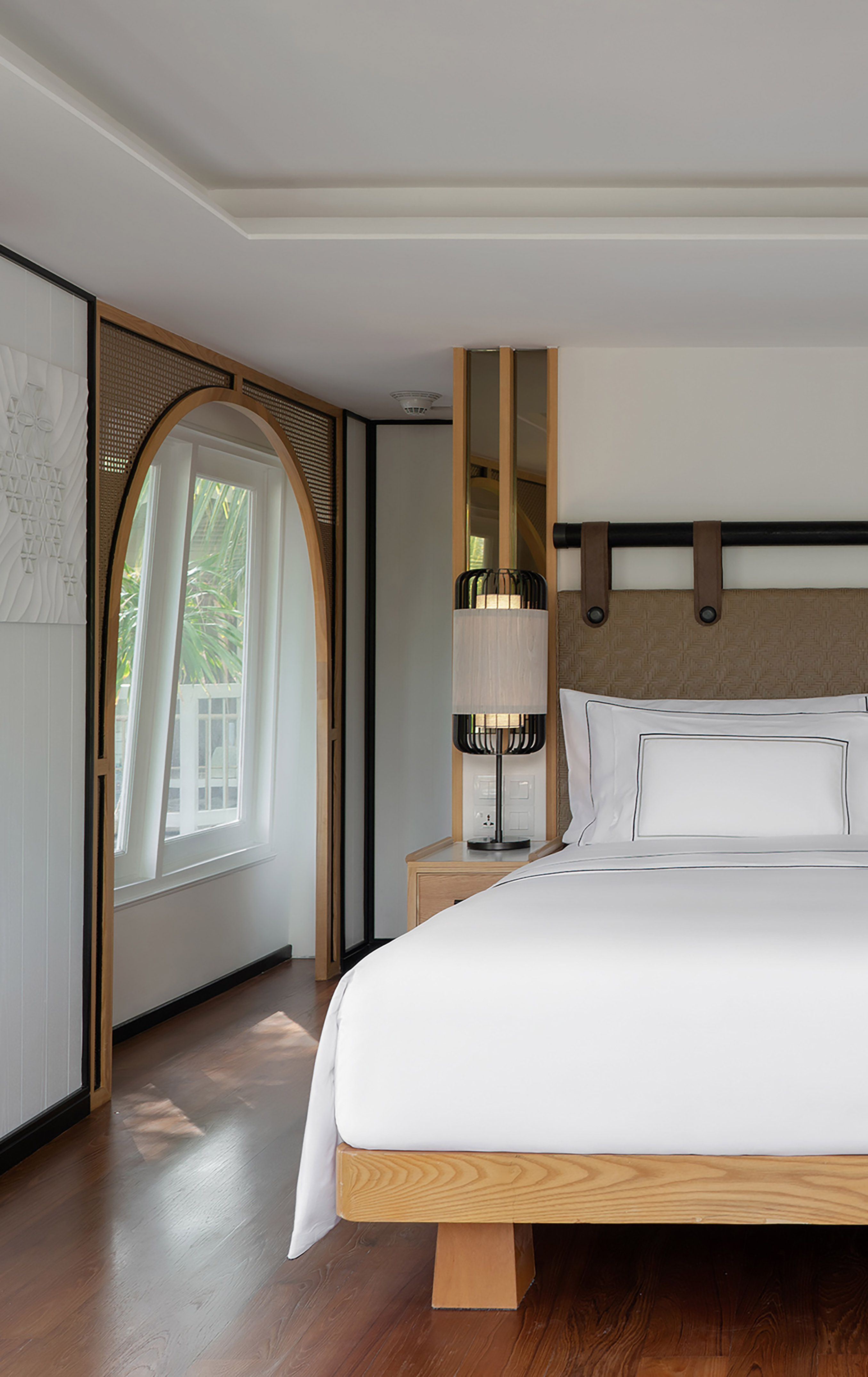 Modern hotel room with white bed, wooden accents, and arched window.