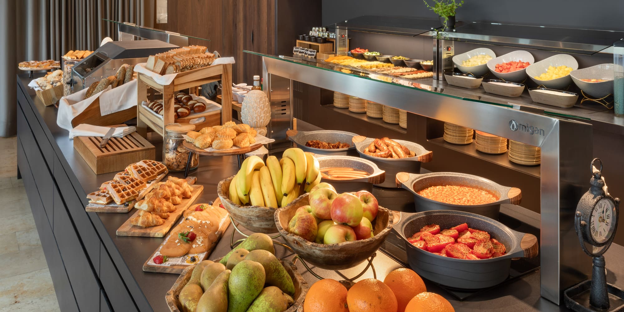 Abundant hotel breakfast buffet with fresh fruits, pastries, hot dishes, and breads.