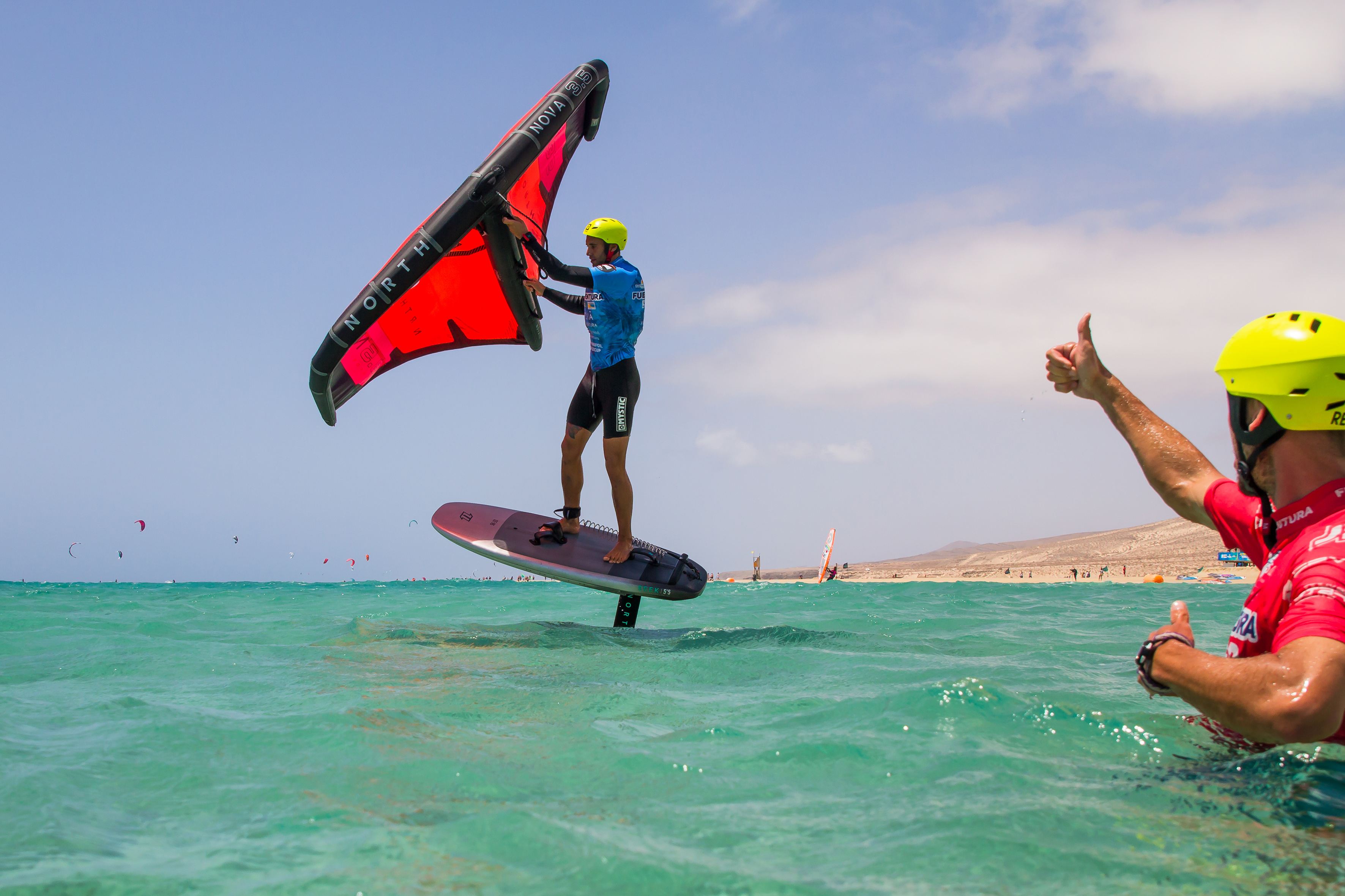 Wing foiler on North Nova hydrofoil board over clear ocean with red wing.