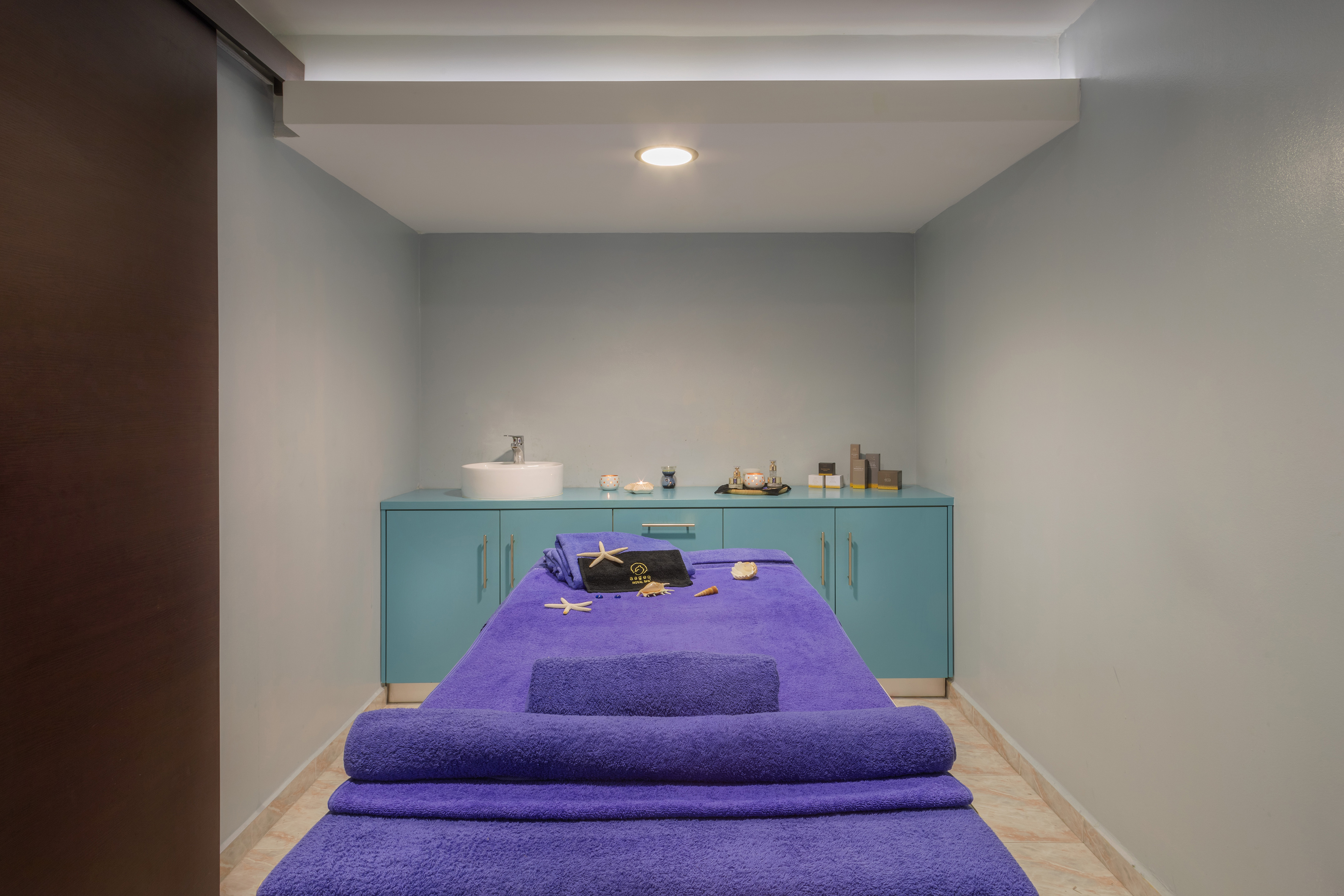Spa room with purple massage table, wellness products, and turquoise cabinet.