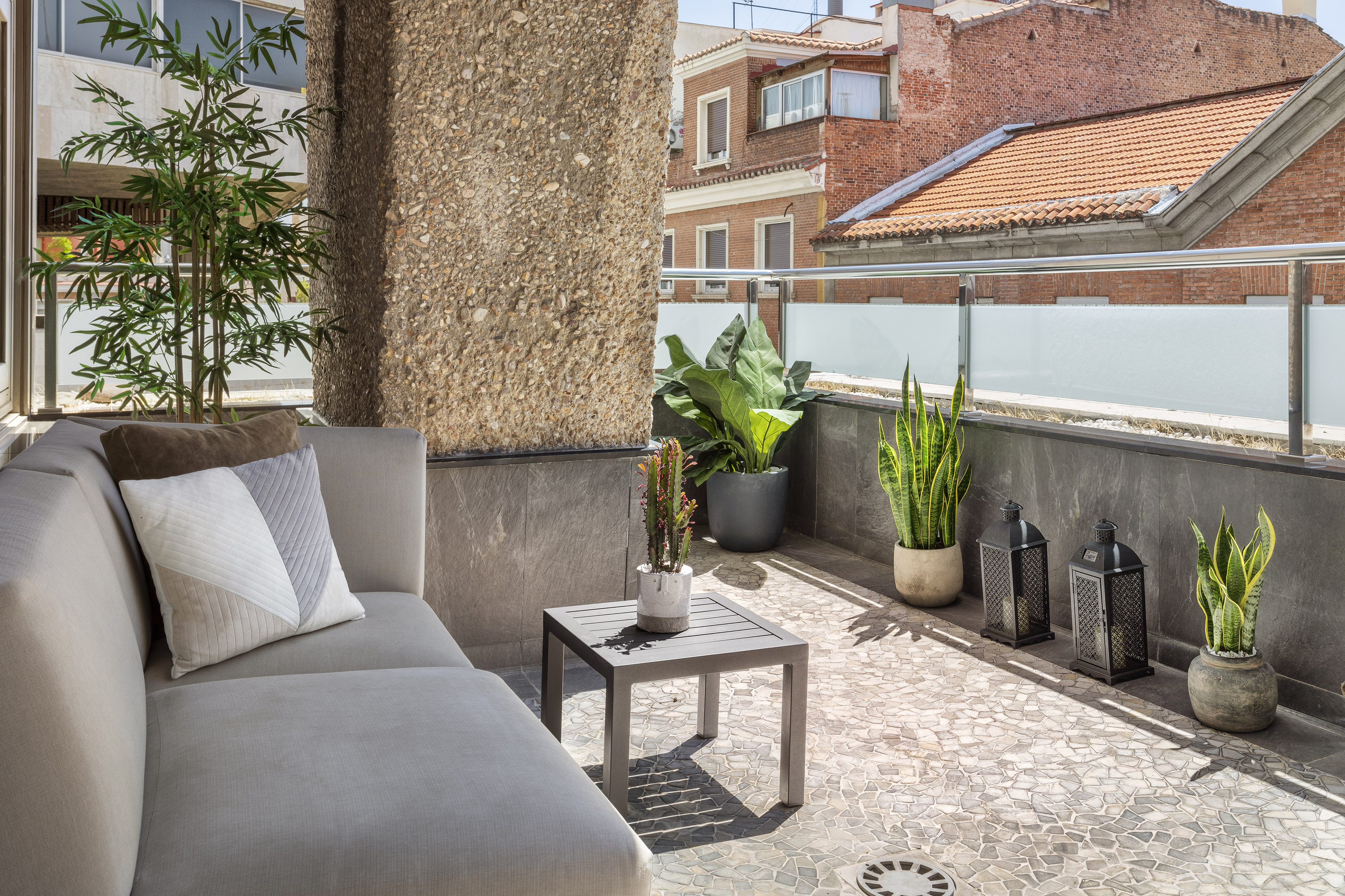 Cozy urban balcony with outdoor sofa, potted plants, side table, and city view.