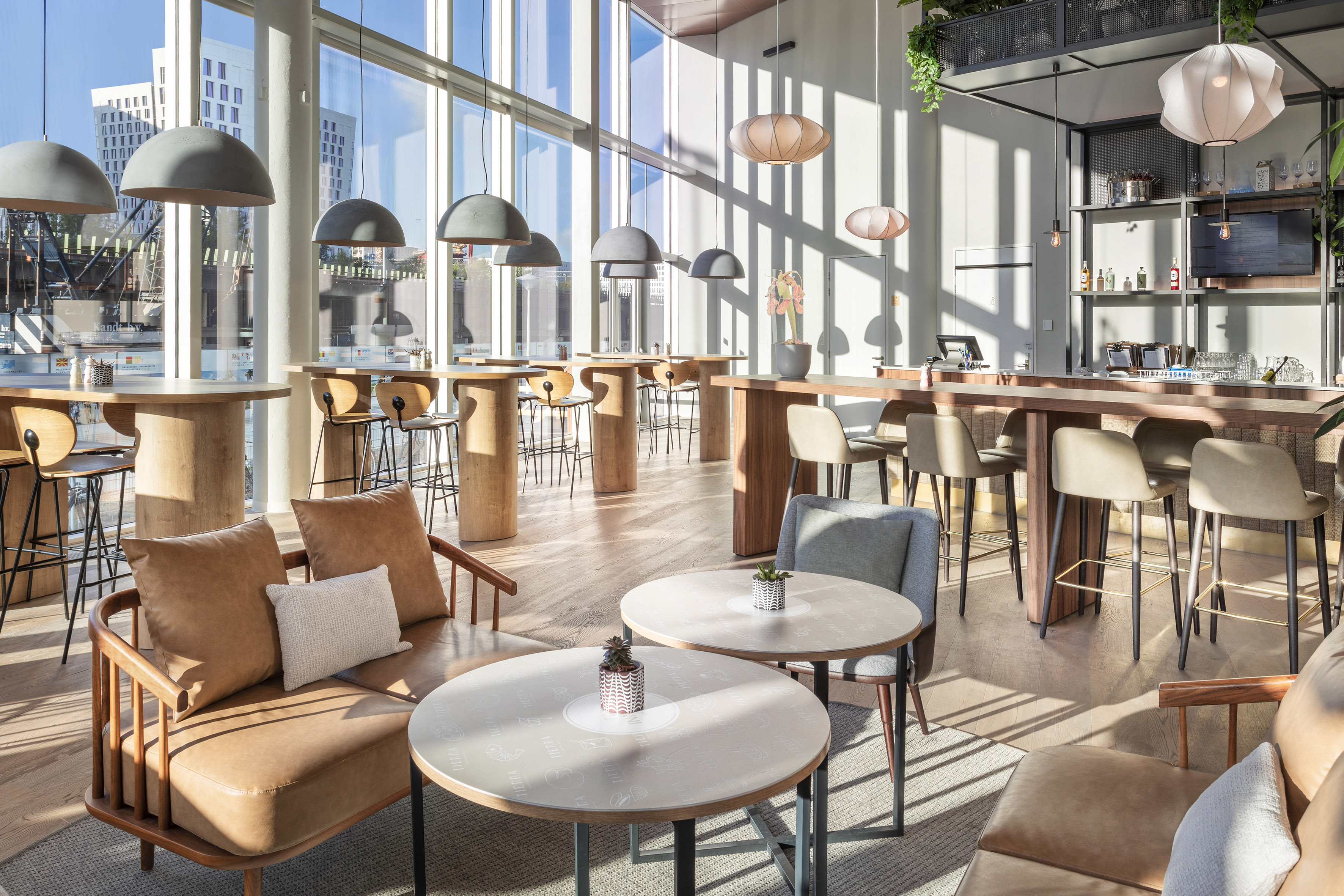 Bright modern lounge with varied seating, bar, and natural light from large windows.