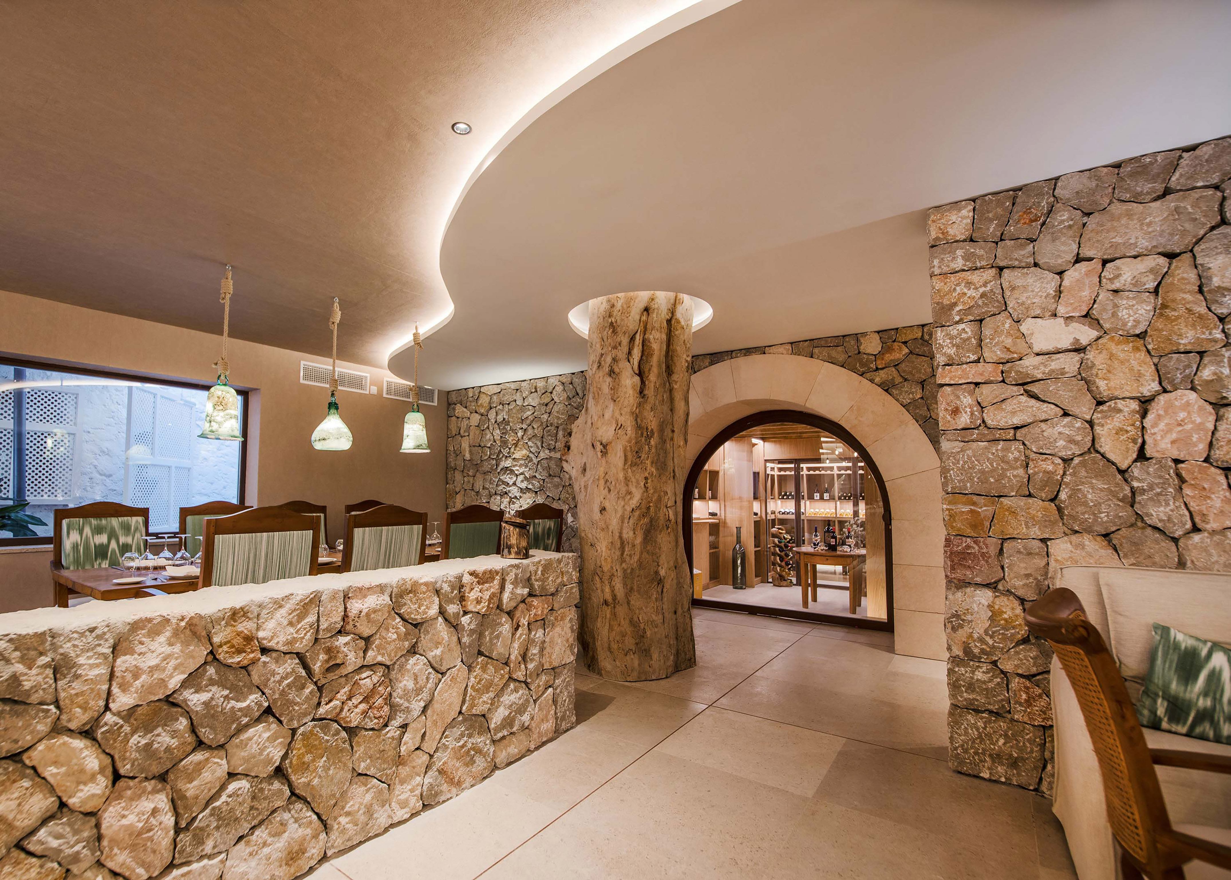 Rustic restaurant dining area with stone walls, tree pillar, and wine cellar arch.
