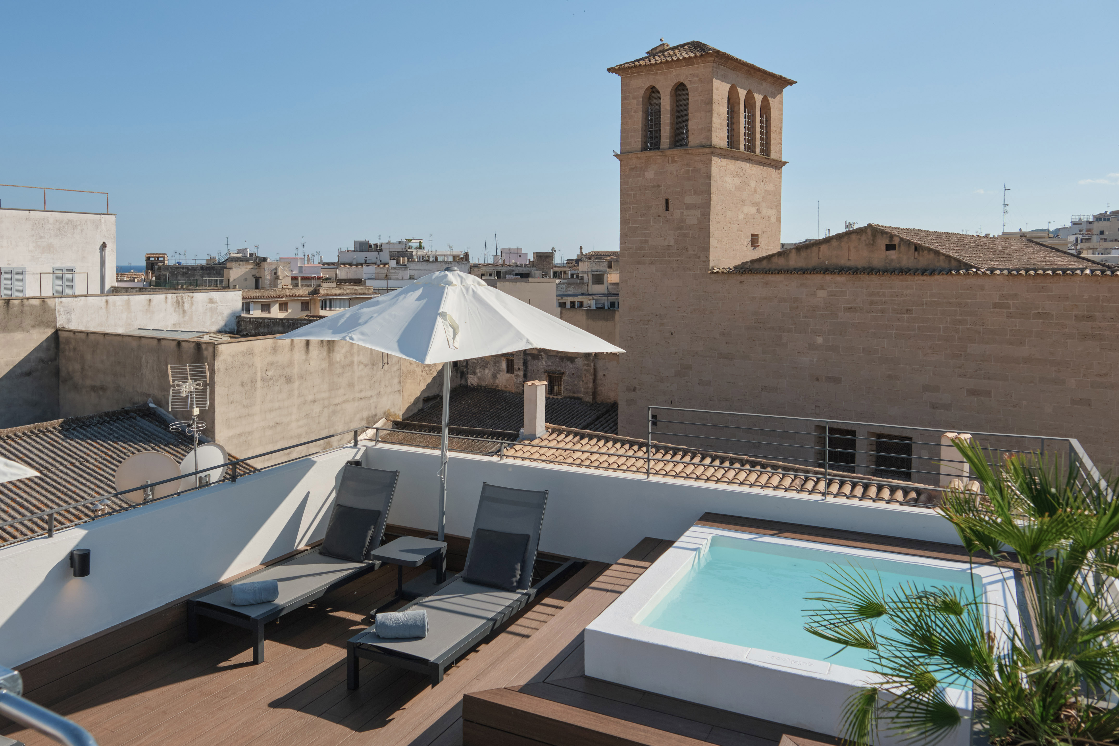 Rooftop terrace with hot tub, loungers, umbrella, and historic city tower view.