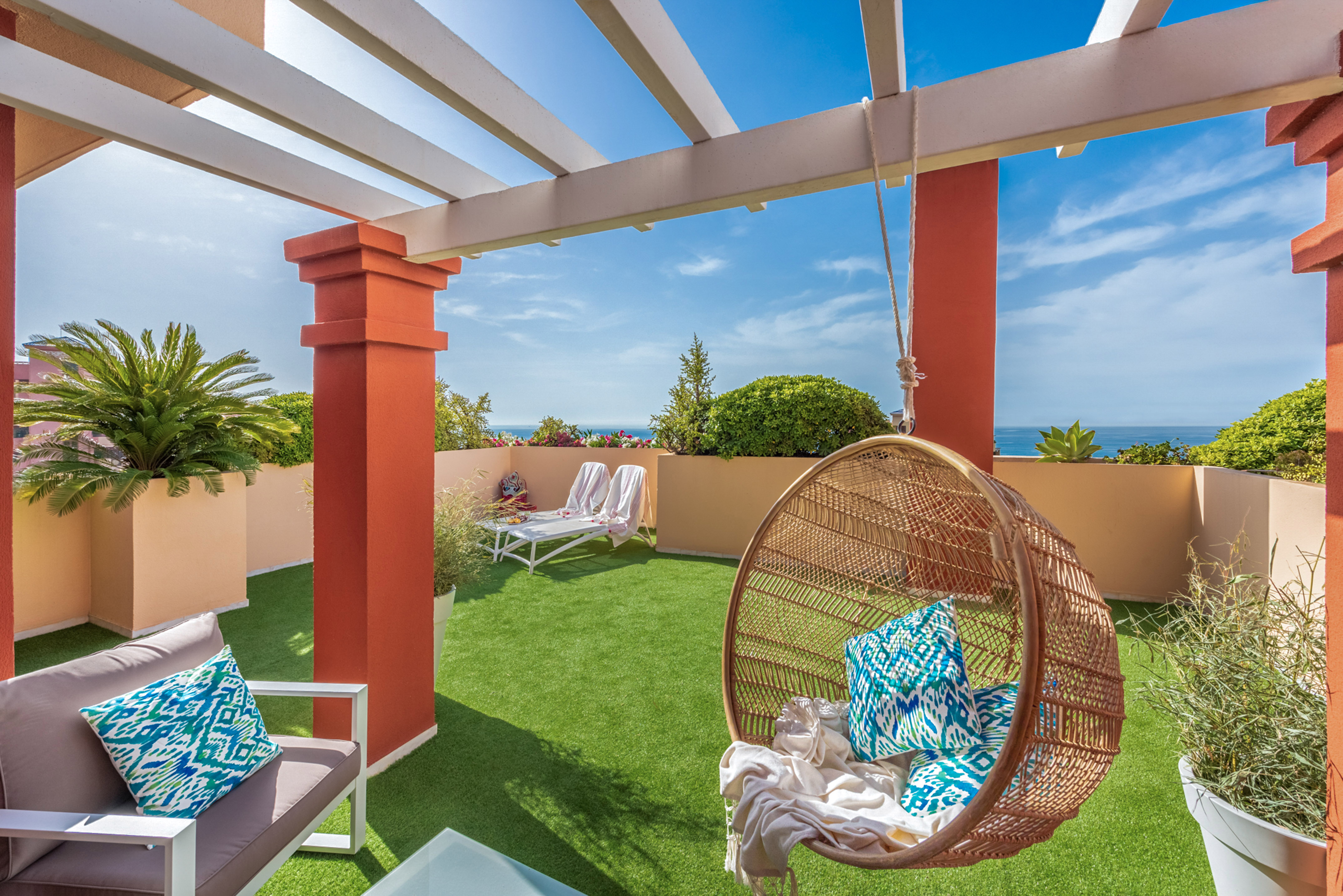 Rooftop terrace with ocean view, pergola, artificial grass, and wicker hanging chair.