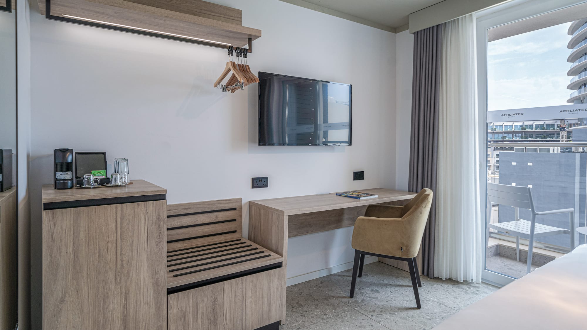 Hotel room with modern desk, wall-mounted TV, coffee corner, and balcony view.