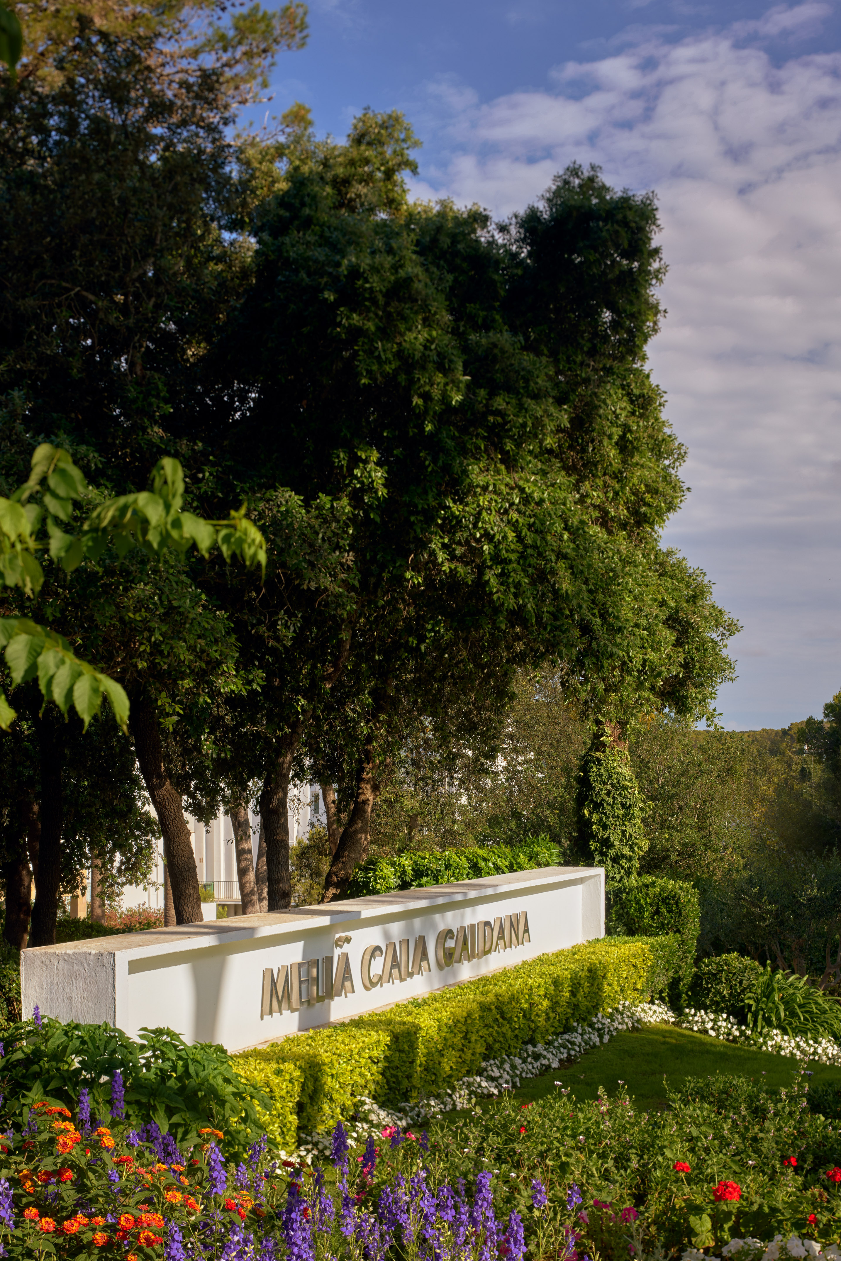 Meliã Cala Gaudana sign among colorful garden flowers and green trees.