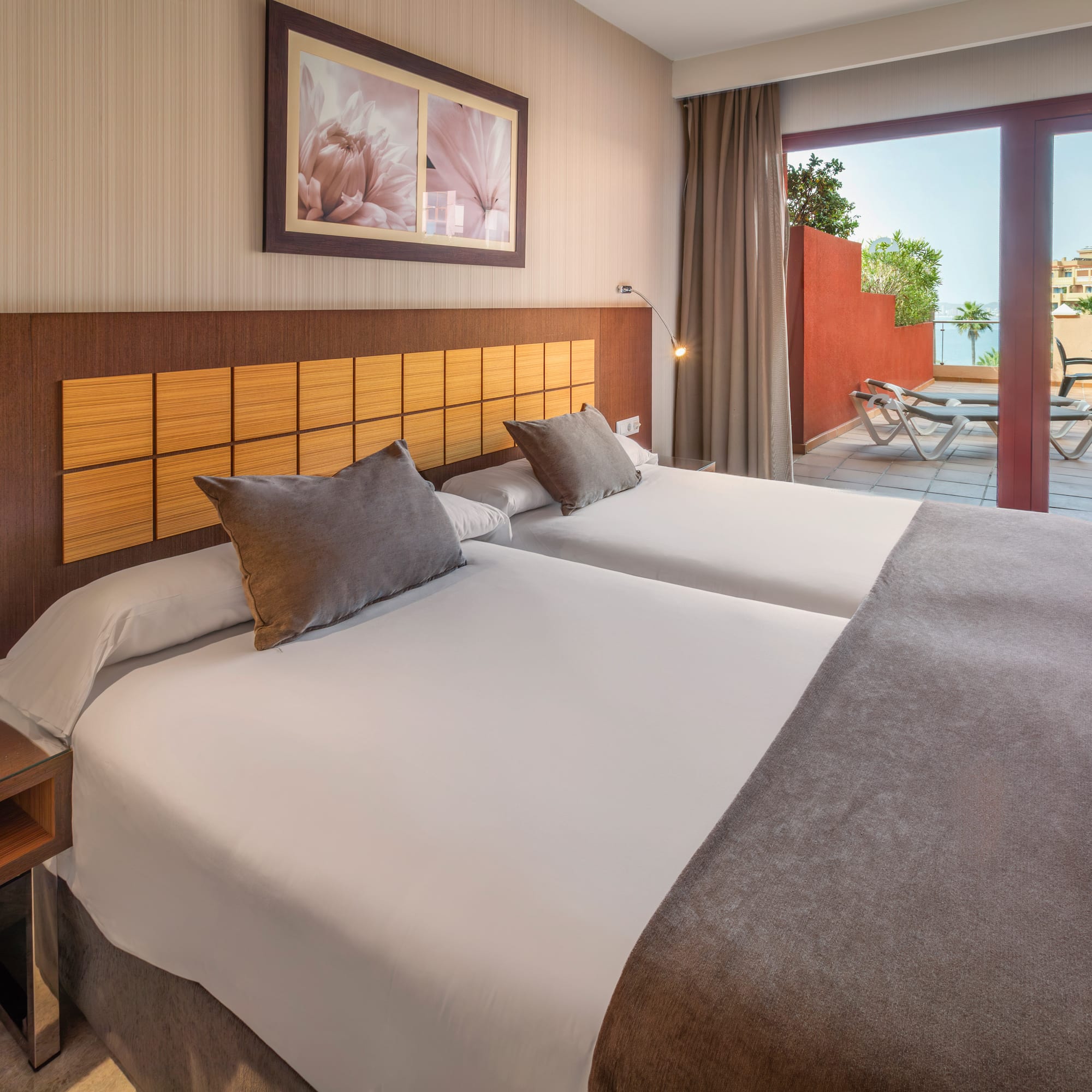 Hotel bedroom with twin beds, private terrace, lounge chairs, and sea view.