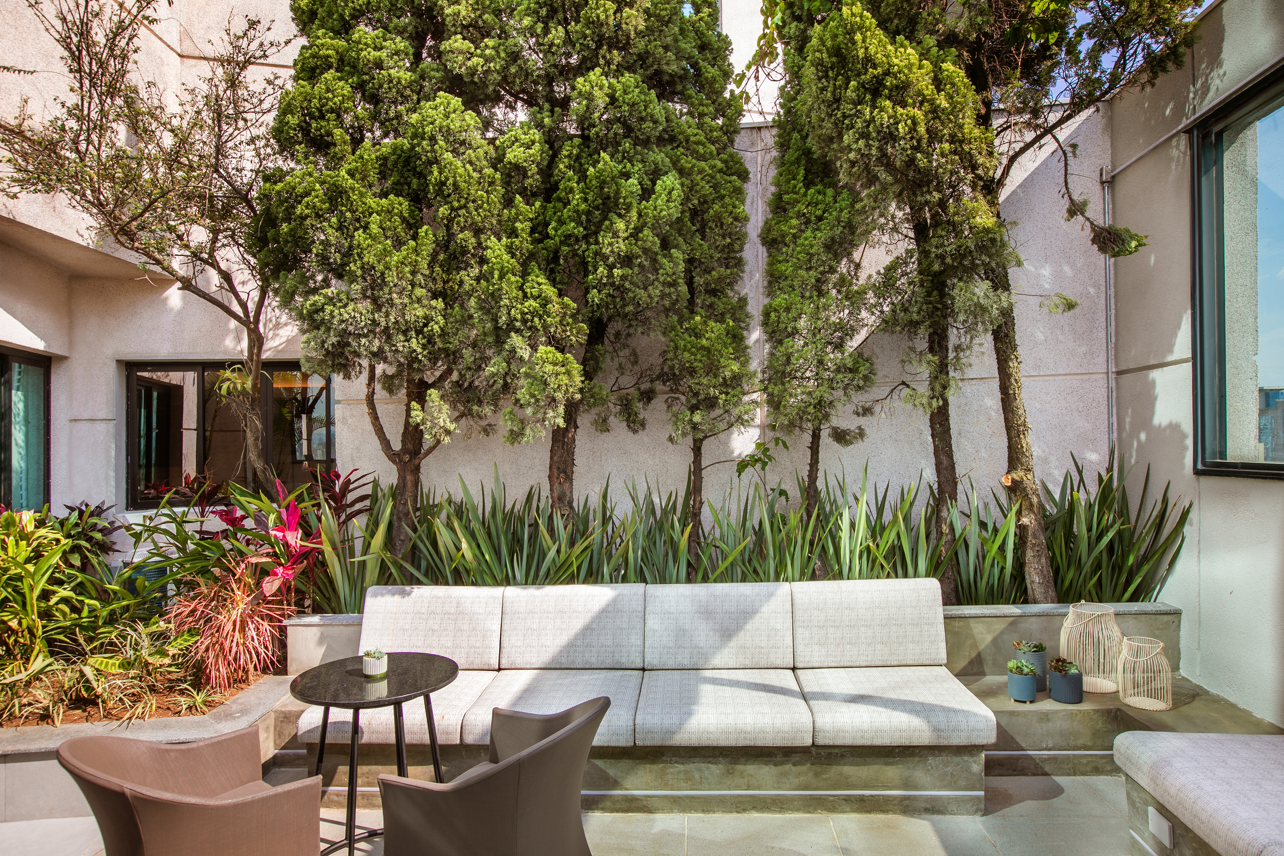Modern outdoor lounge with sofa, chairs, and lush green garden plants.