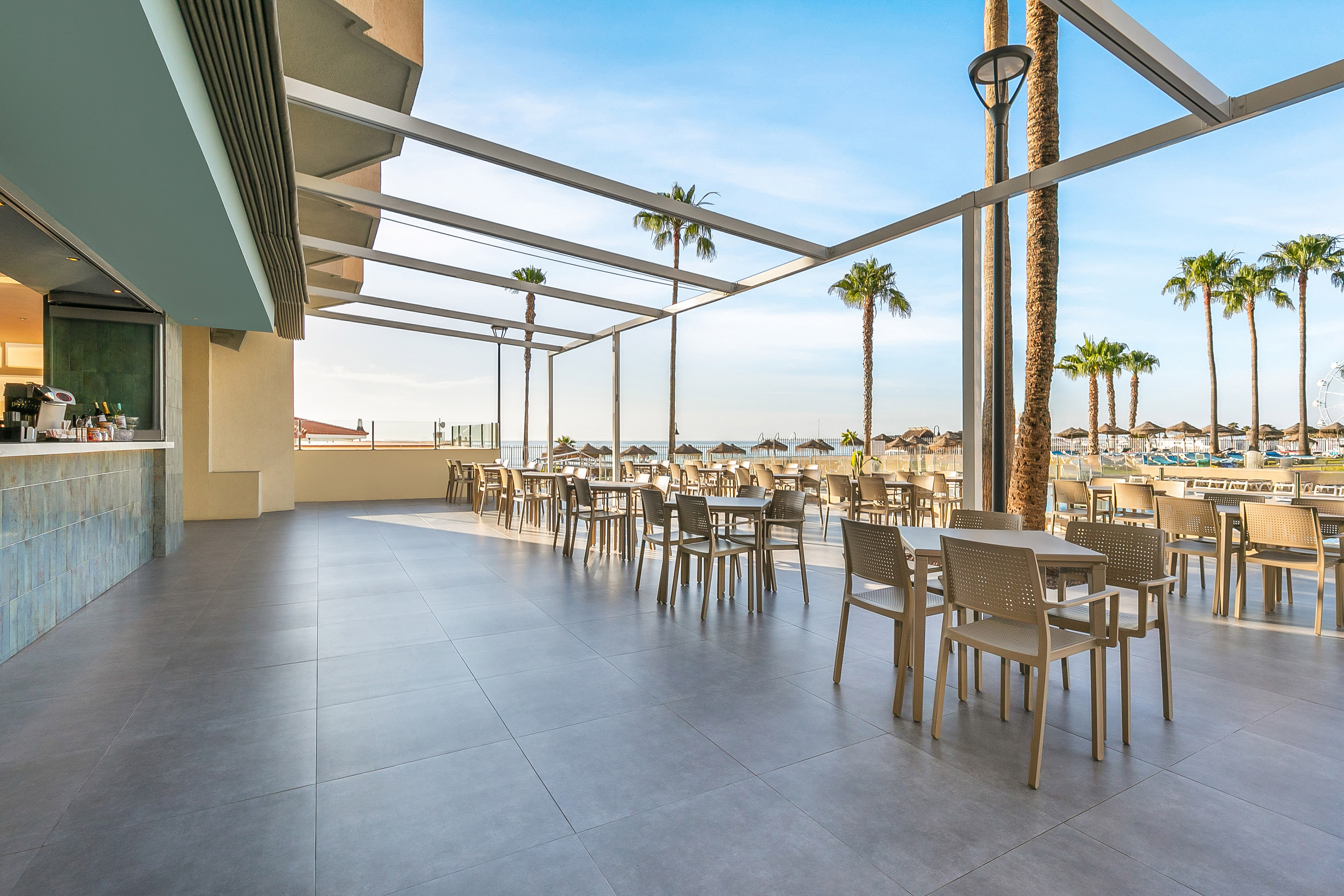 Hotel patio restaurant overlooking beach with palm trees and ocean.