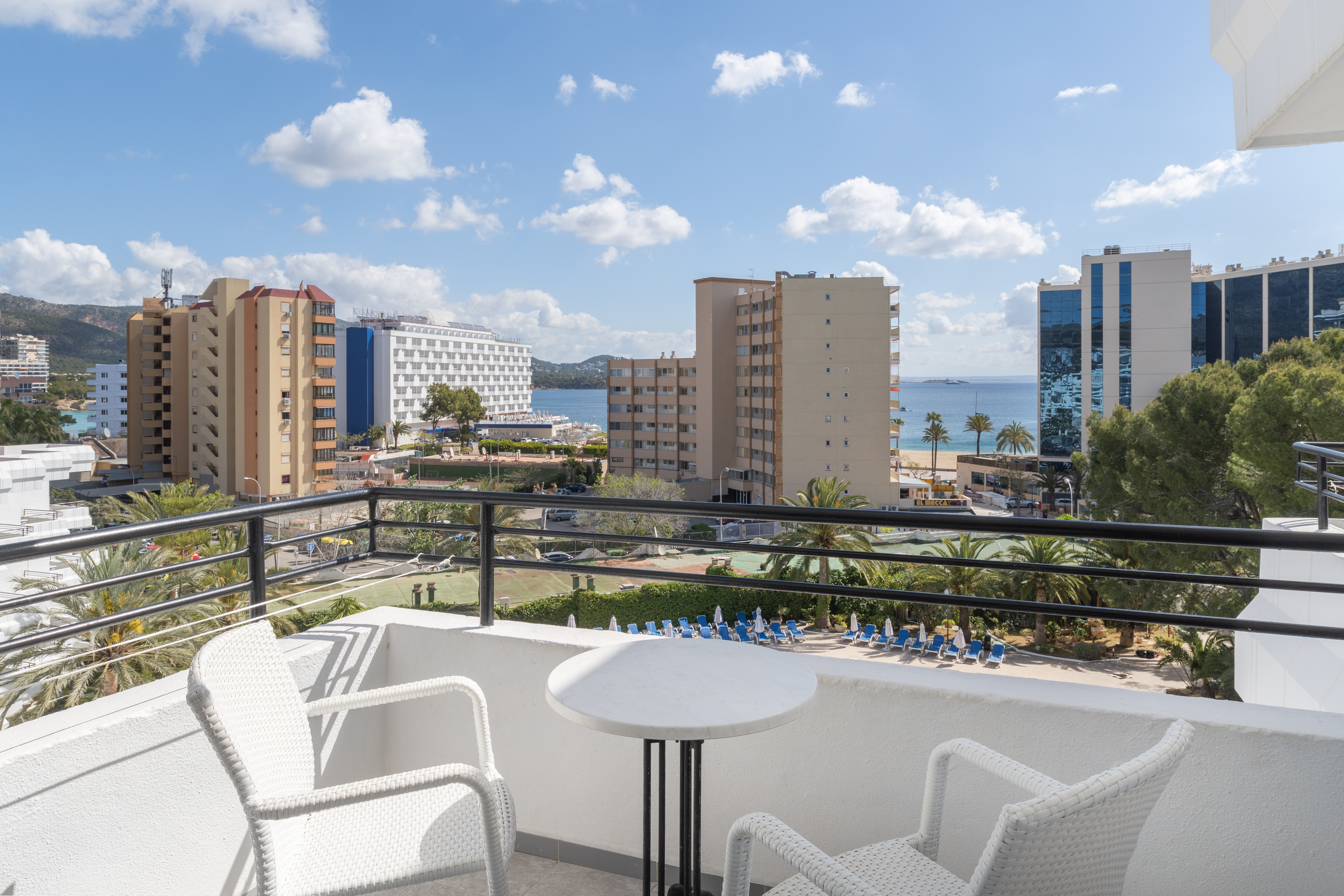 Sunny hotel balcony with sea view, overlooking coastal city and beach.