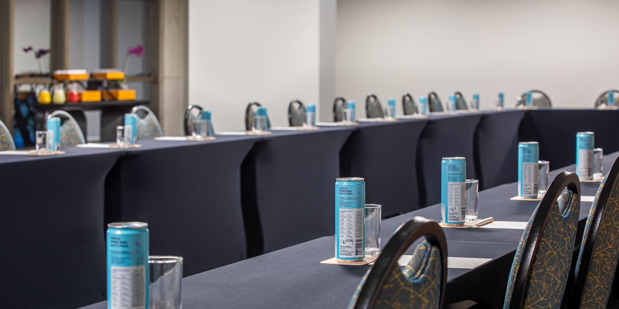 Conference room tables with mineral water cans, glasses, and notepads for a meeting.