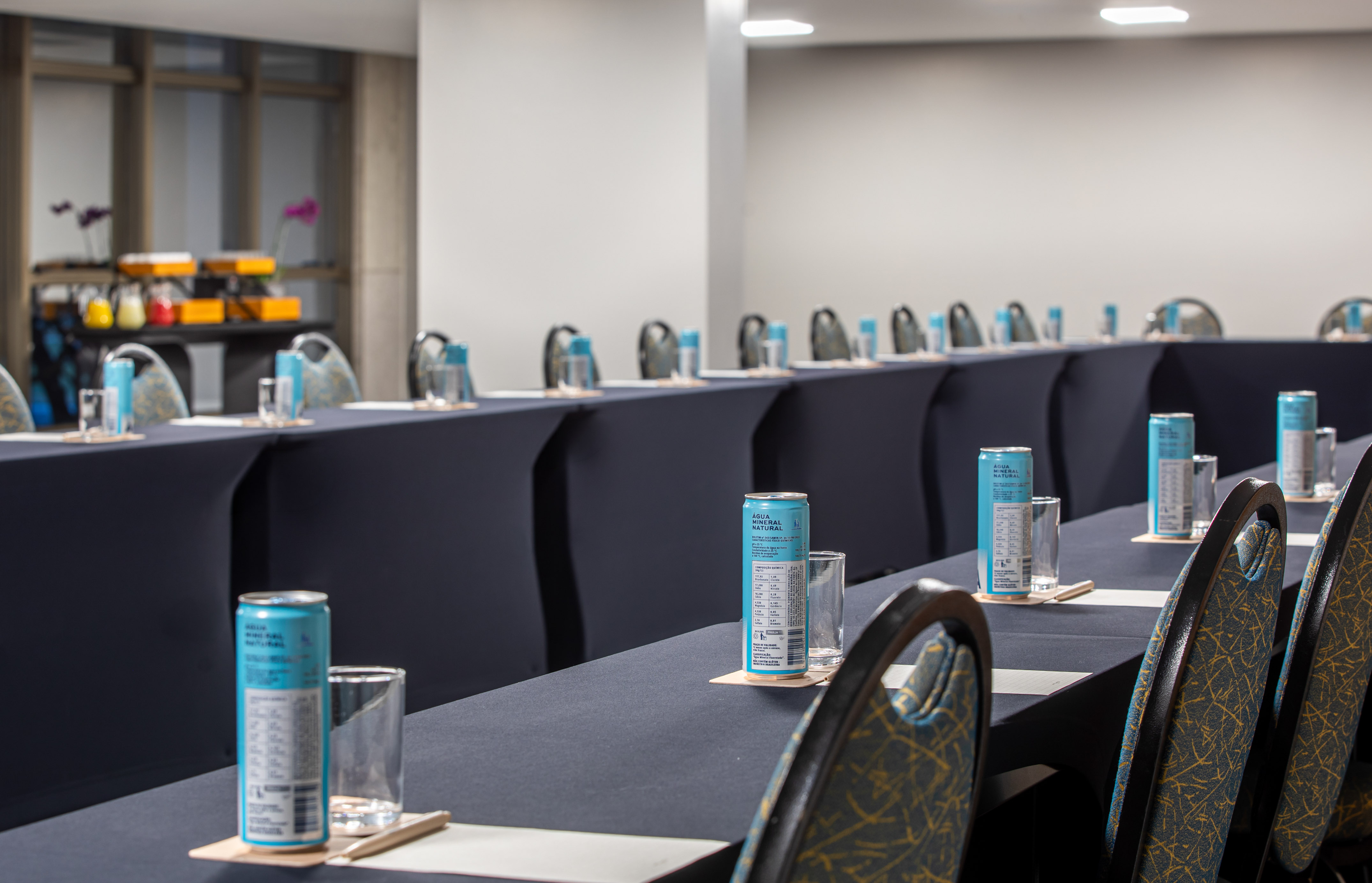 Conference room tables with mineral water cans, glasses, and notepads for a meeting.