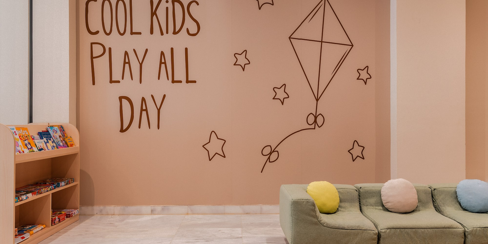 Children's play space with 'Cool Kids Play All Day' mural, sofa, bookshelf.