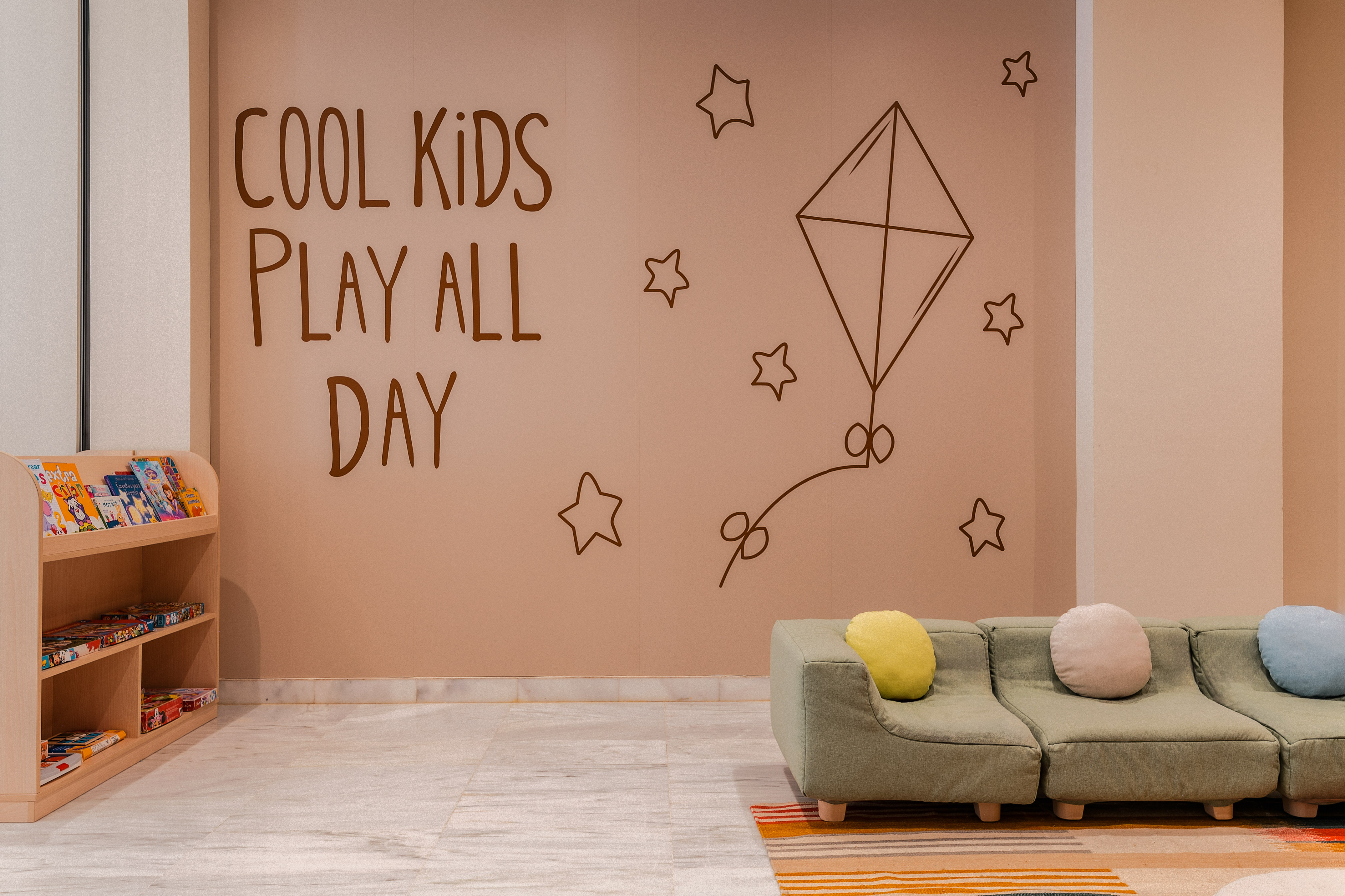 Children's play space with 'Cool Kids Play All Day' mural, sofa, bookshelf.