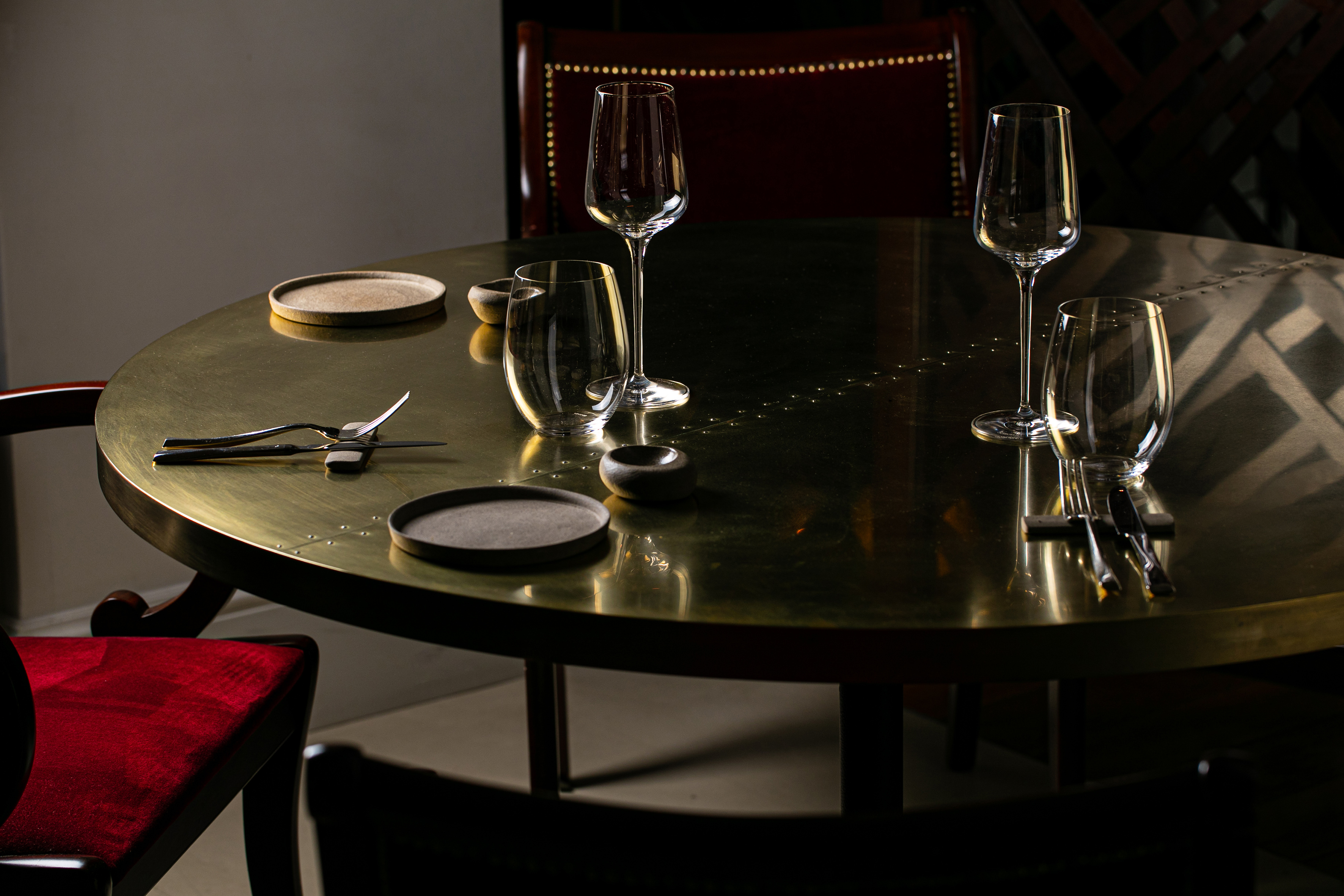 Elegant brass restaurant table set with wine glasses, plates, and cutlery in dark ambiance.