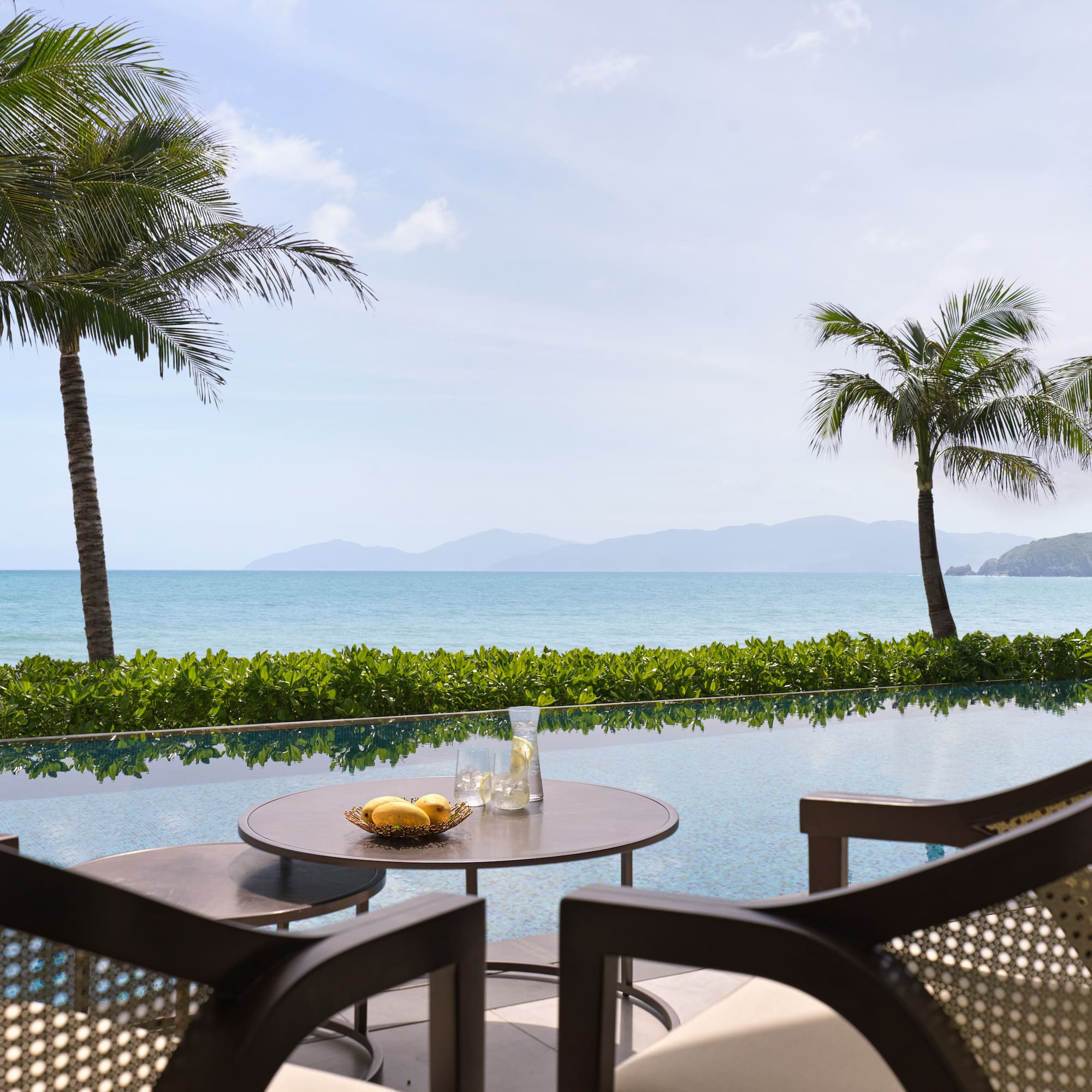 a table and chairs with a view of the ocean and palm trees