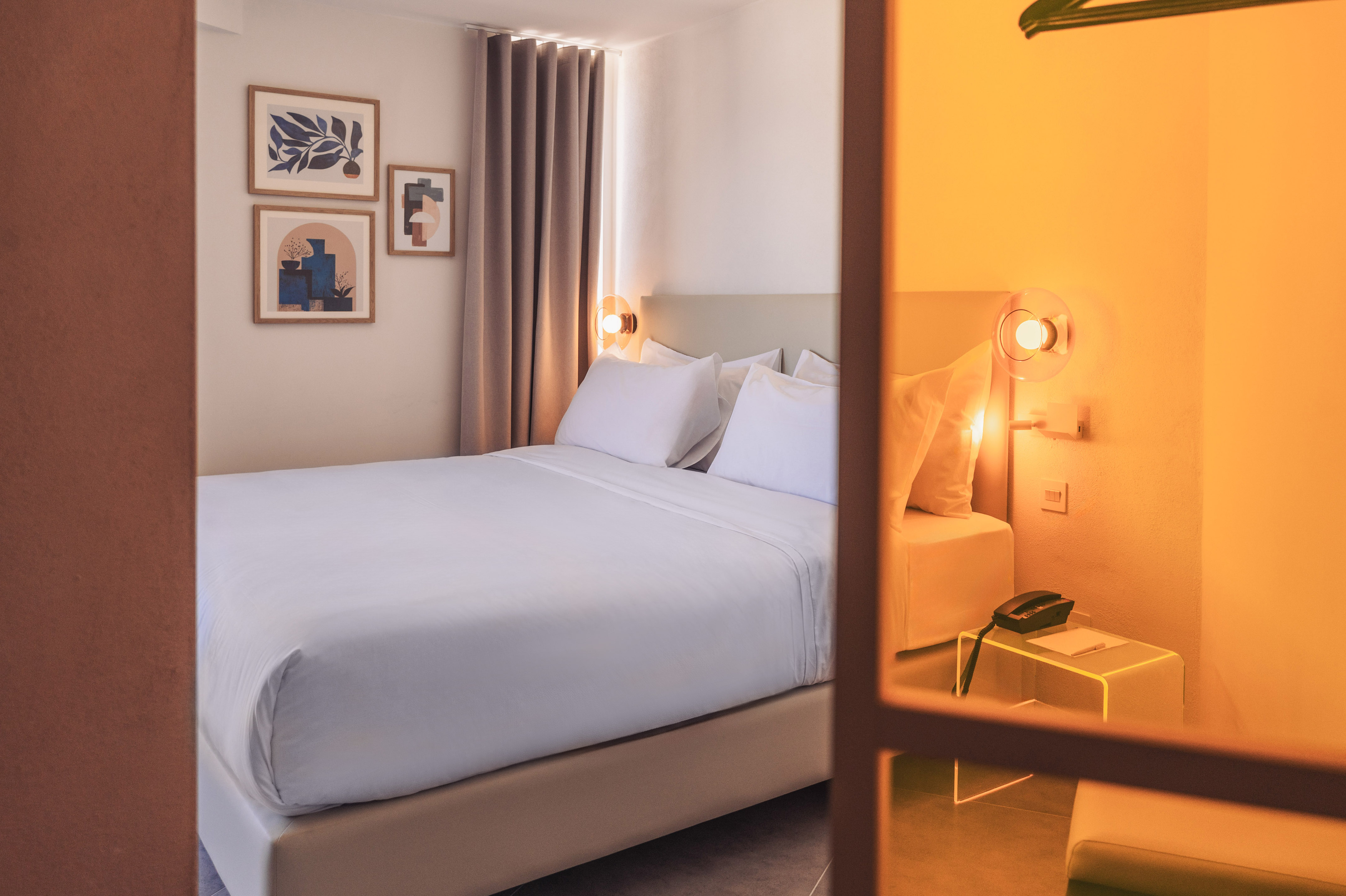 Modern hotel bedroom with white bed, abstract wall art, and warm lighting.