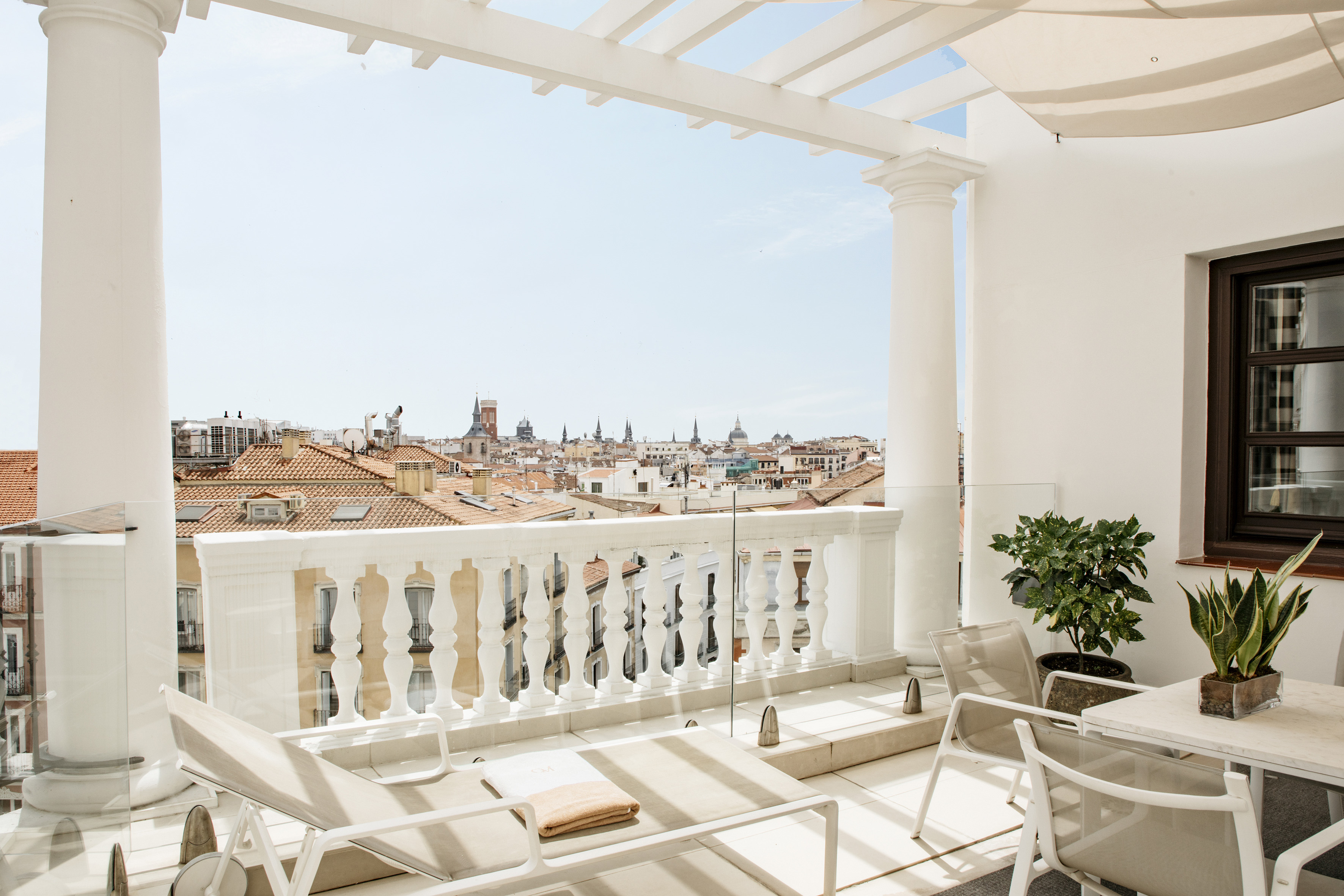 Rooftop terrace with lounge chairs and Madrid city skyline view over red roofs.