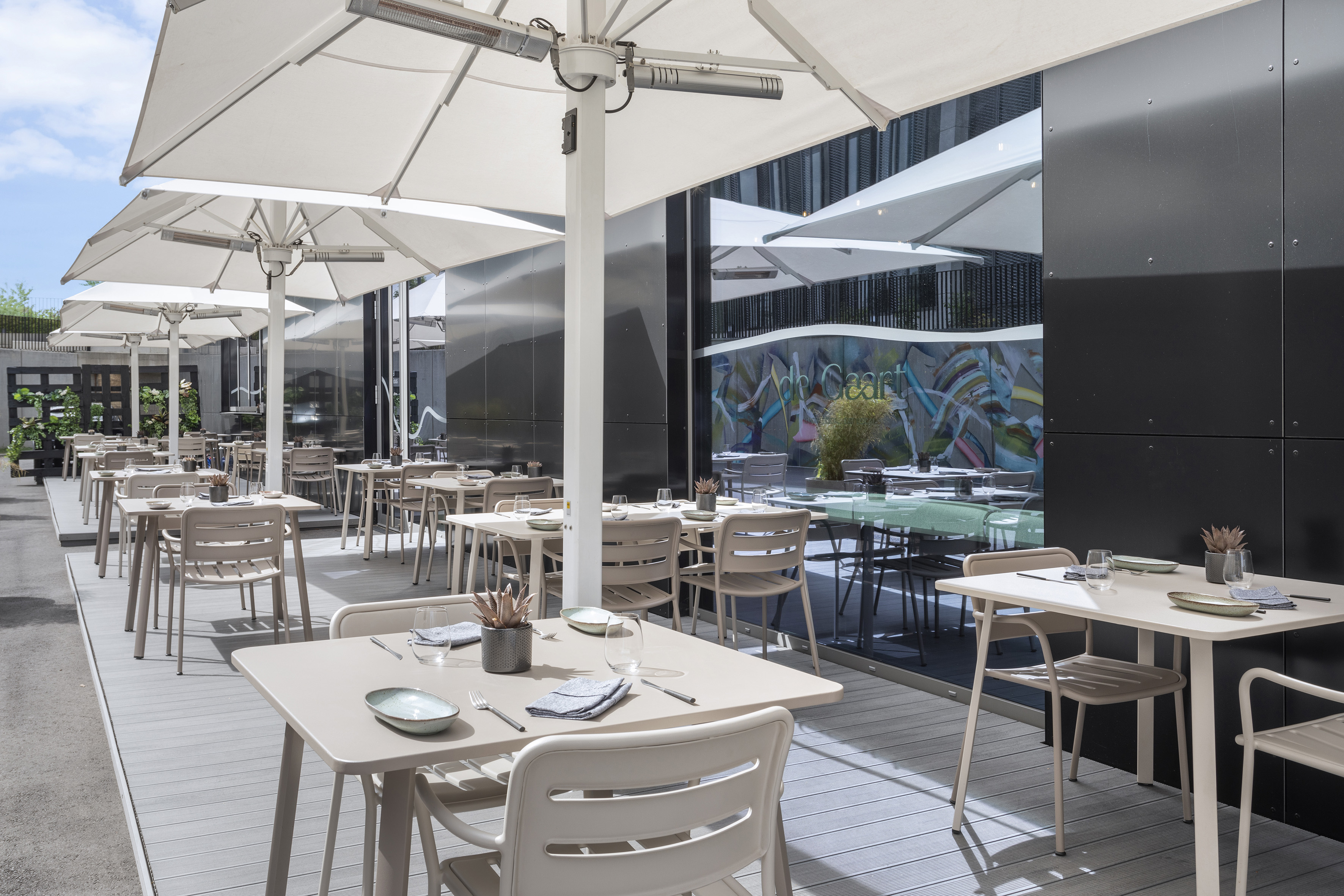 Modern outdoor dining patio with beige tables, chairs, and white umbrellas.