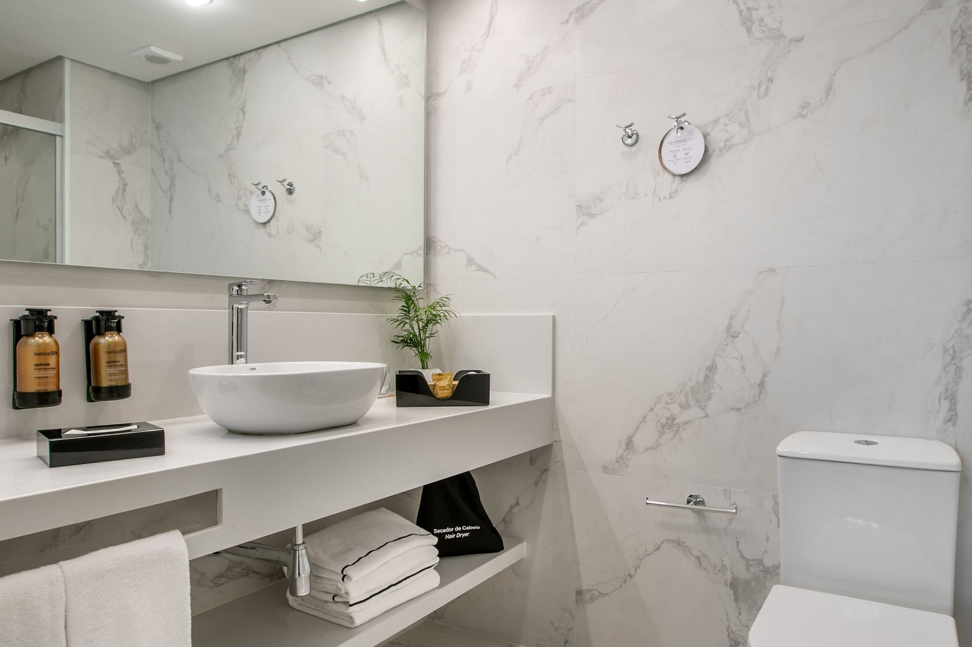 Modern white marble bathroom with vessel sink, large mirror, and toilet.