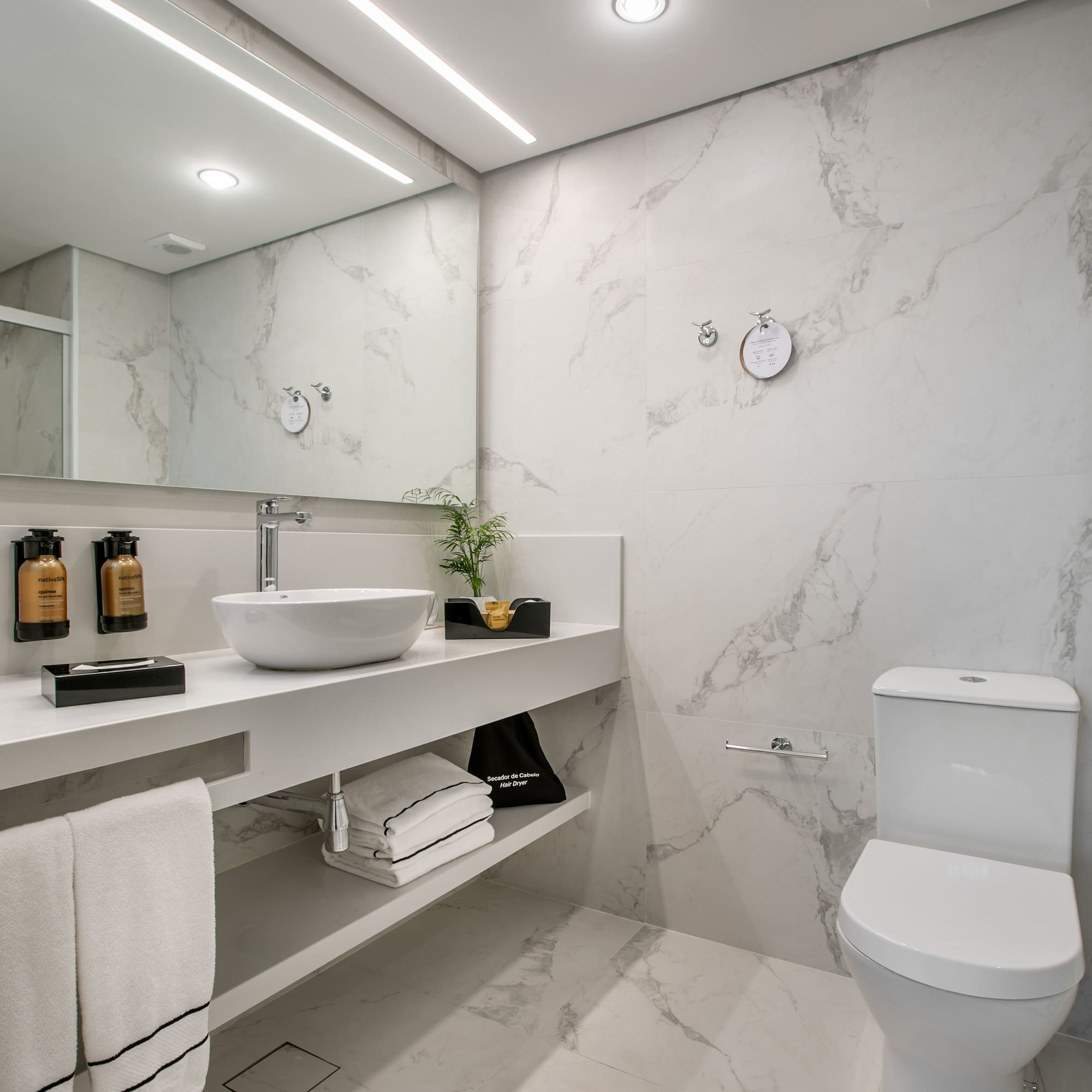 Modern white marble bathroom with vessel sink, large mirror, and toilet.