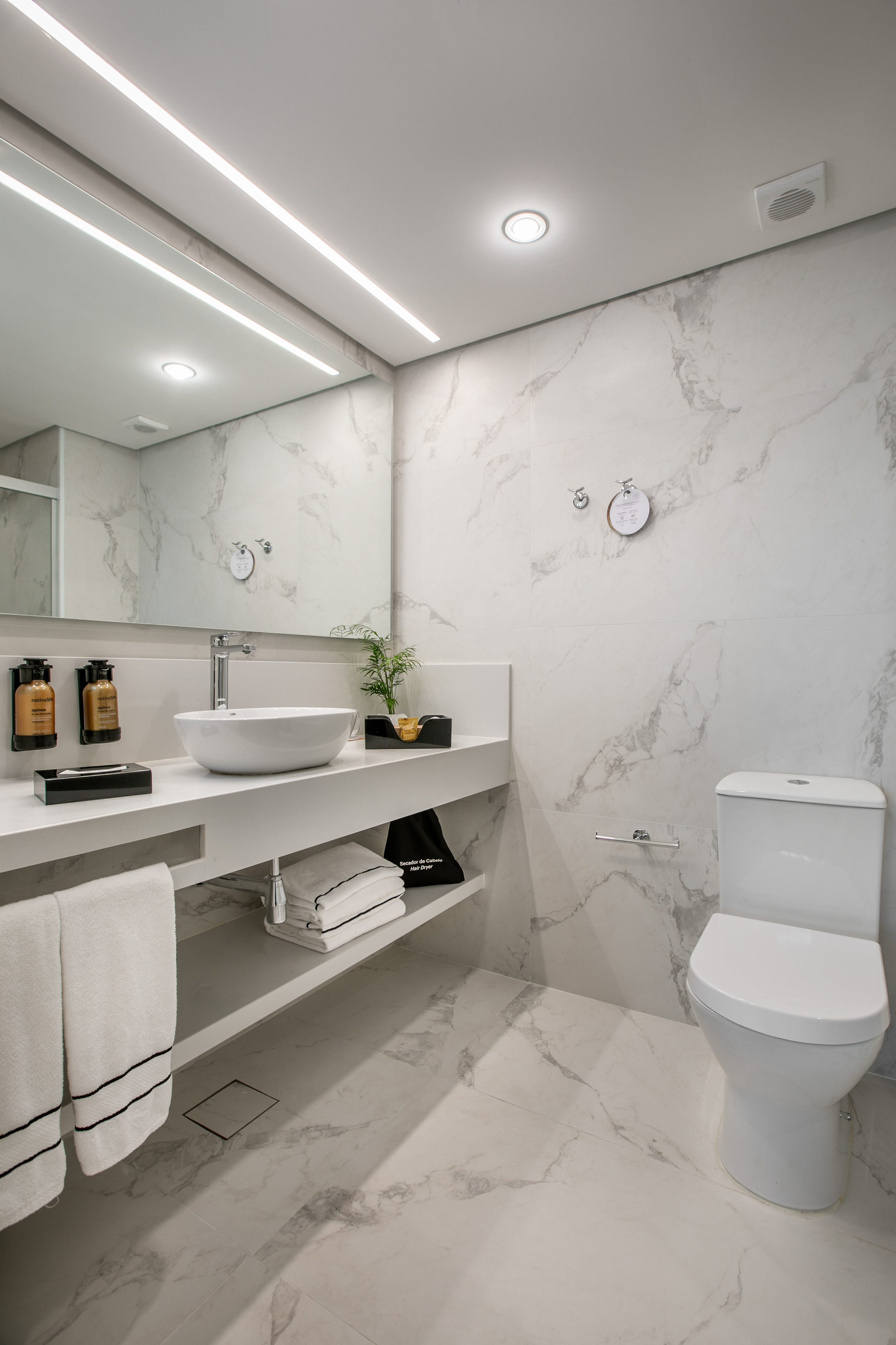 Modern white marble bathroom with vessel sink, large mirror, and toilet.