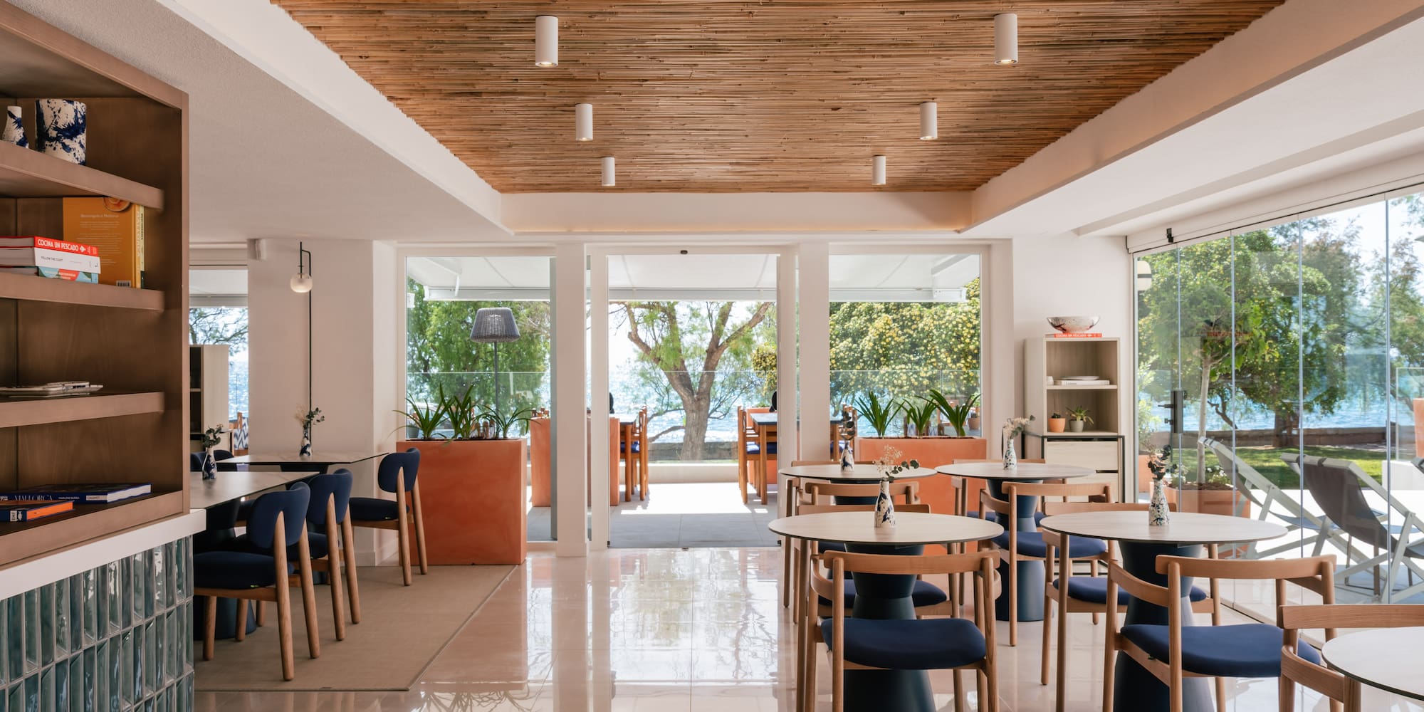 Modern restaurant interior with bamboo ceiling, blue chairs, and sea view.
