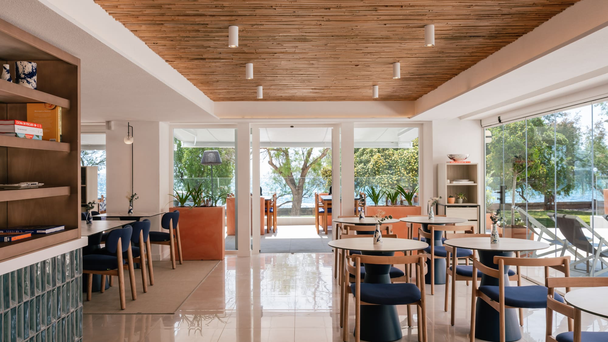 Modern restaurant interior with bamboo ceiling, blue chairs, and sea view.