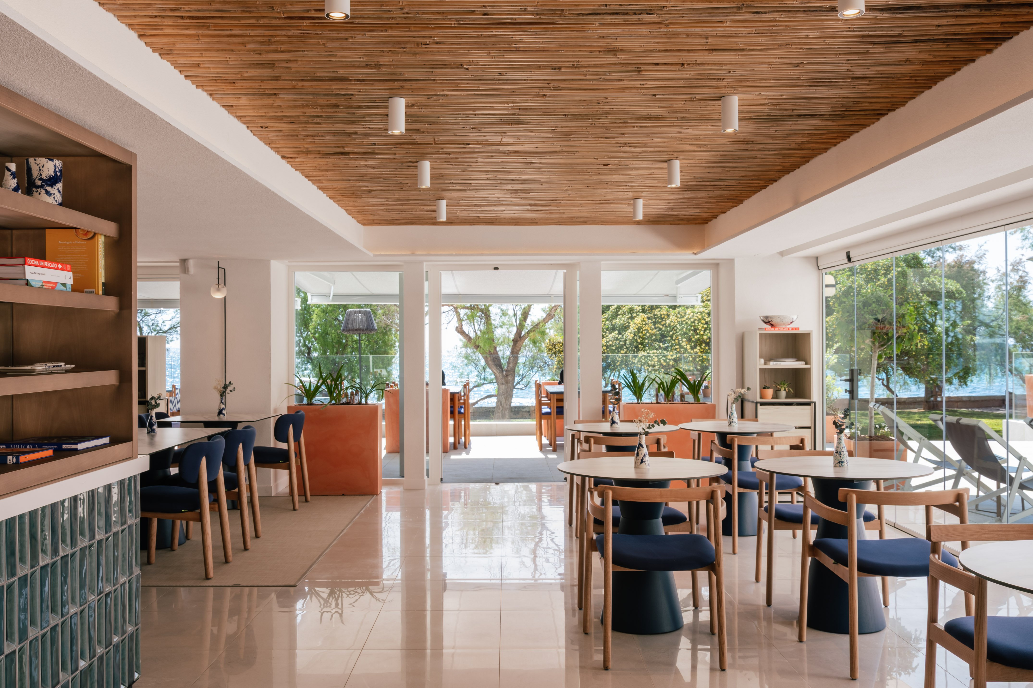 Modern restaurant interior with bamboo ceiling, blue chairs, and sea view.