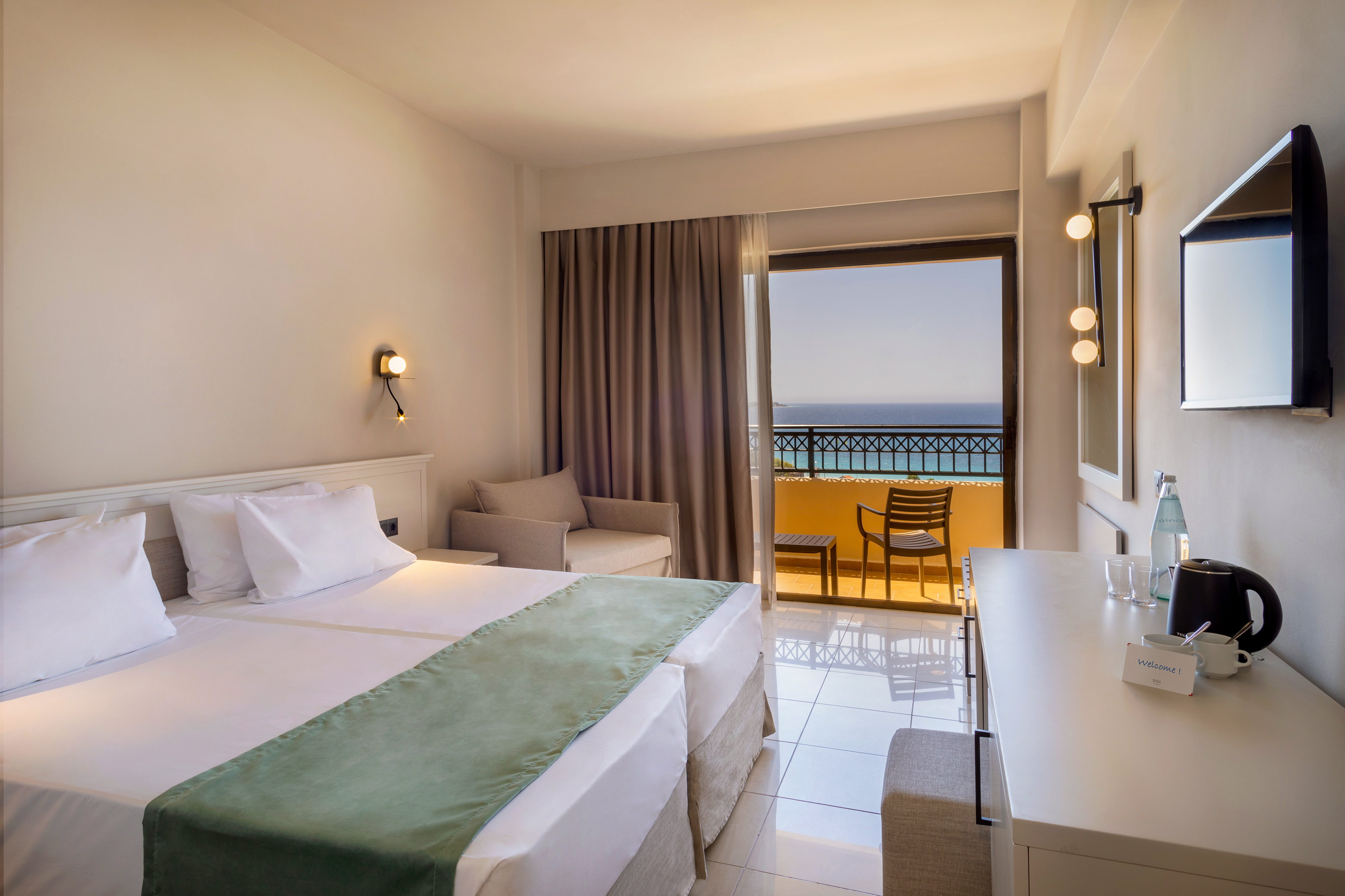 Modern hotel room with double bed and balcony overlooking the sea.