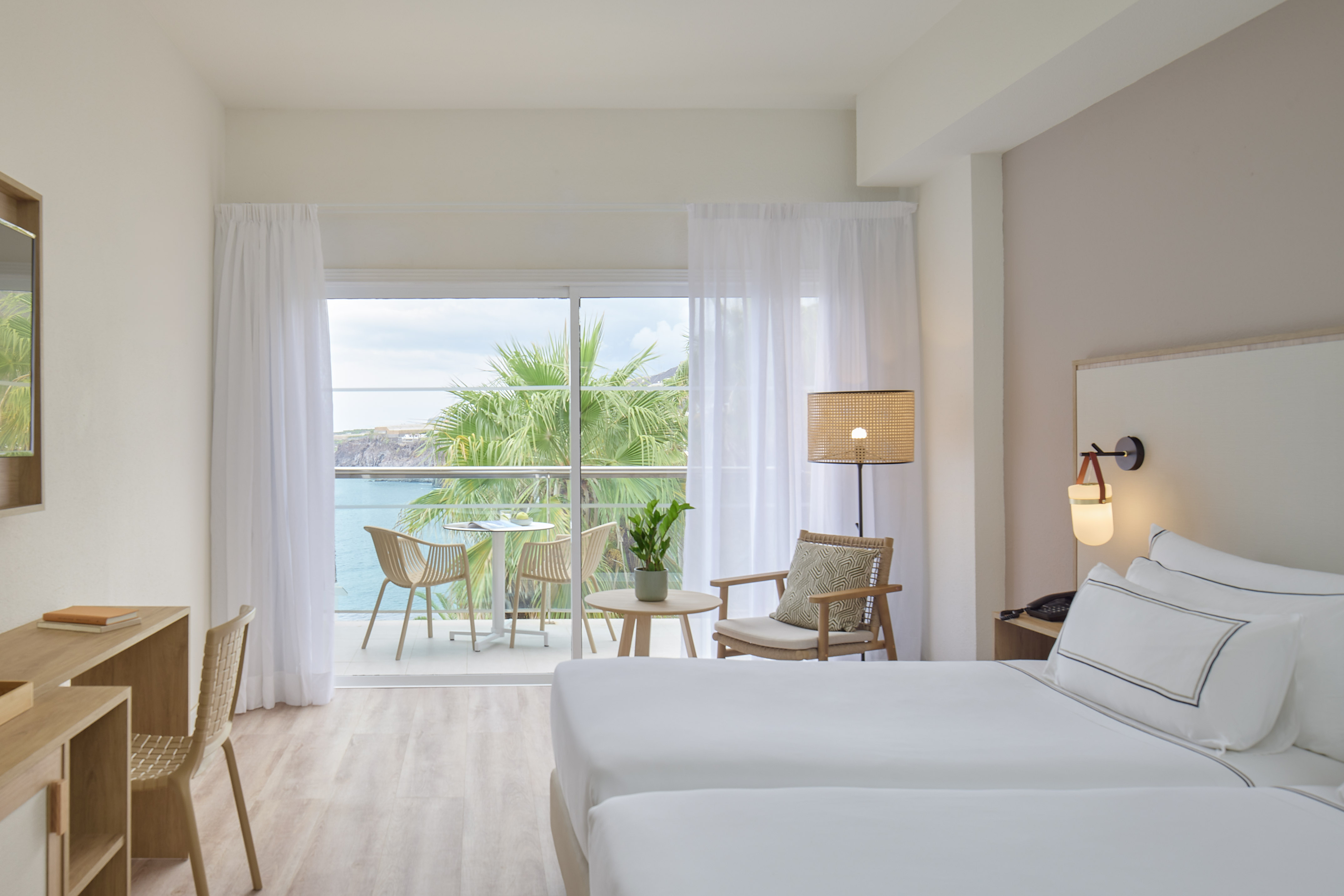 Bright hotel room with ocean view balcony, palm trees, and modern decor.