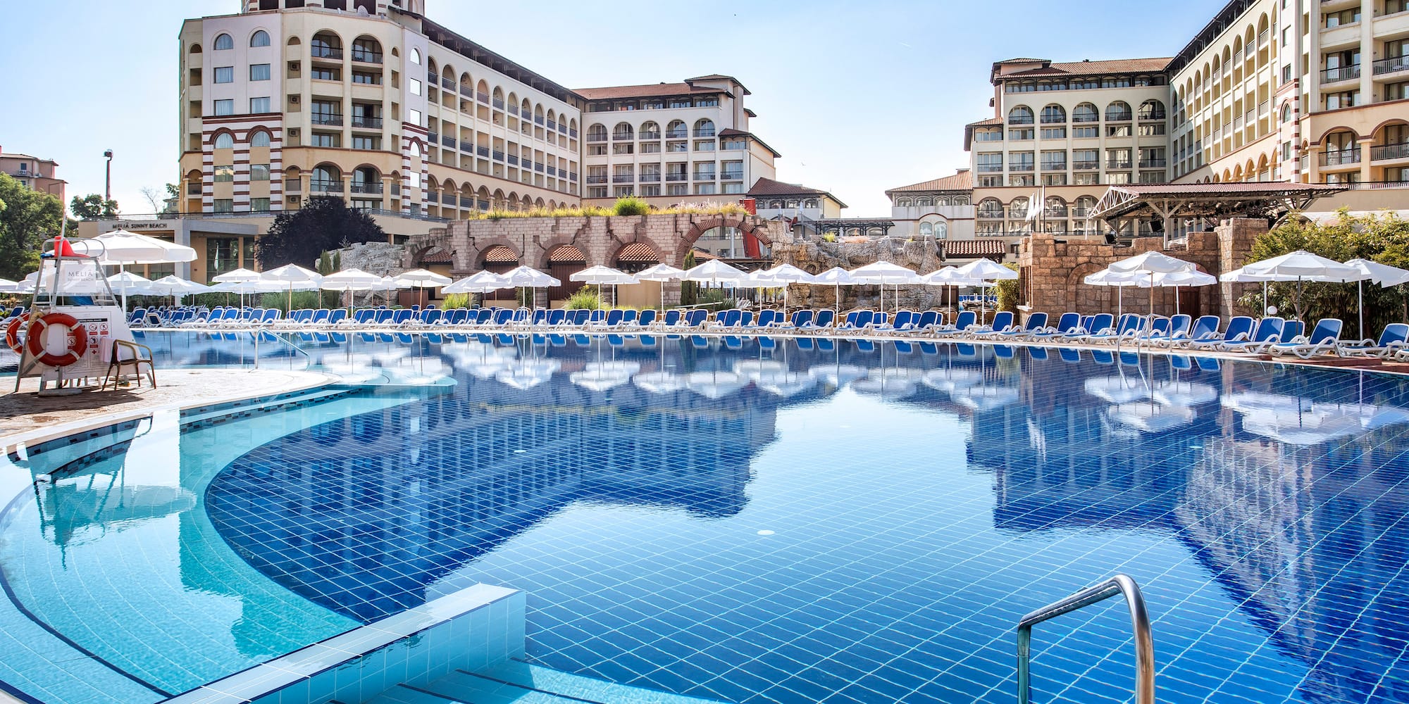 a pool with umbrellas and chairs in front of buildings