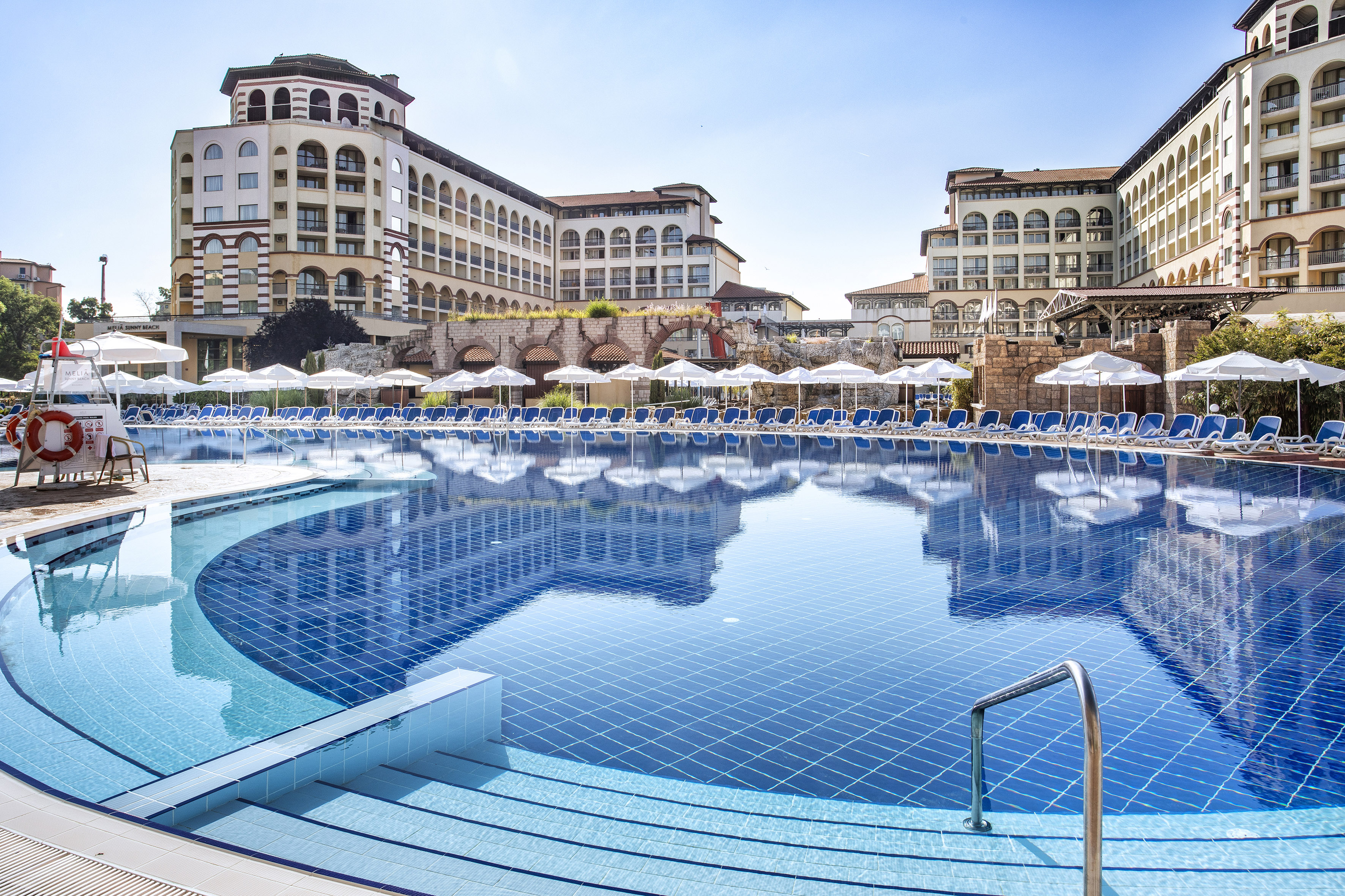 a pool with umbrellas and chairs in front of buildings