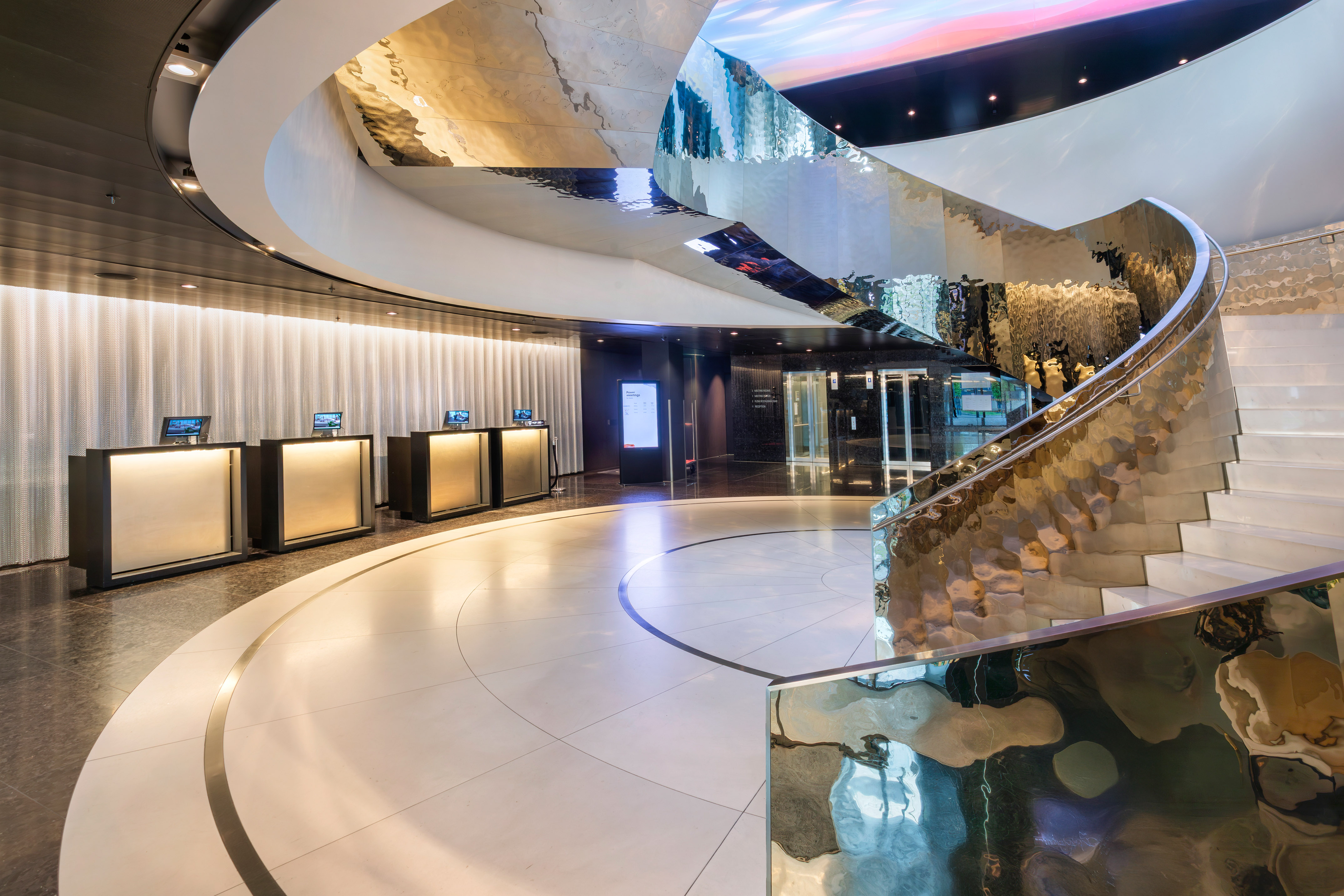 Luxury hotel lobby with modern spiral staircase, reflective walls, and reception.
