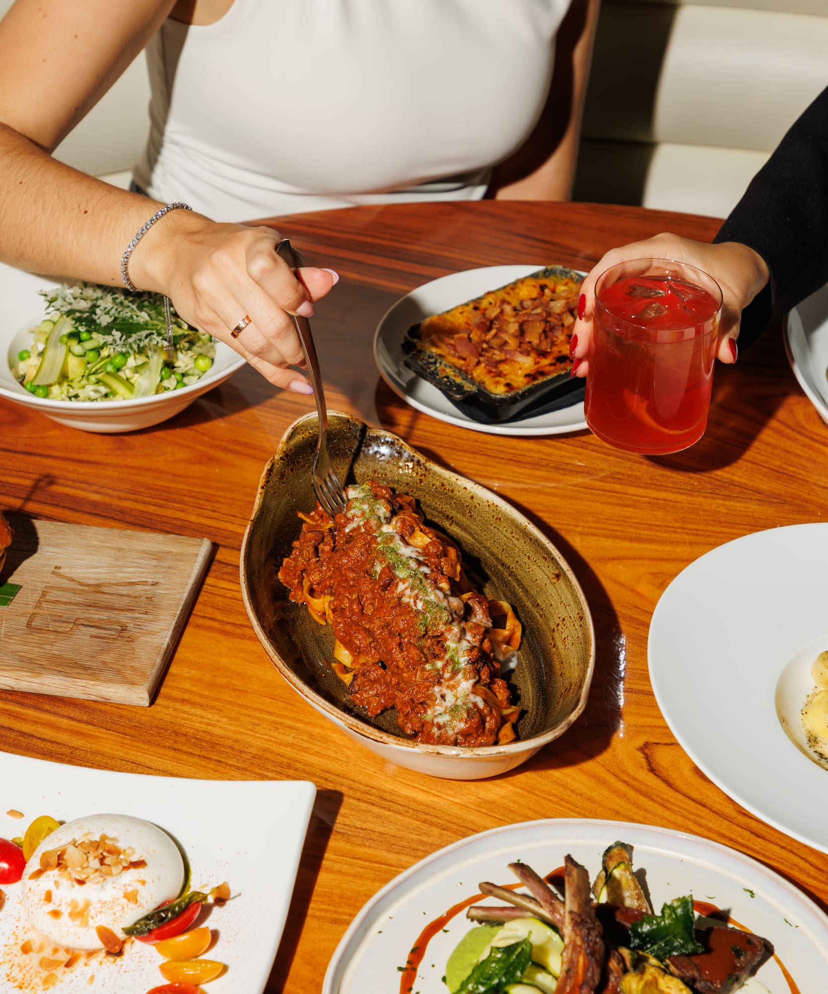 Table of Italian dishes: pasta bolognese, burrata, lamb chops, and cocktails.