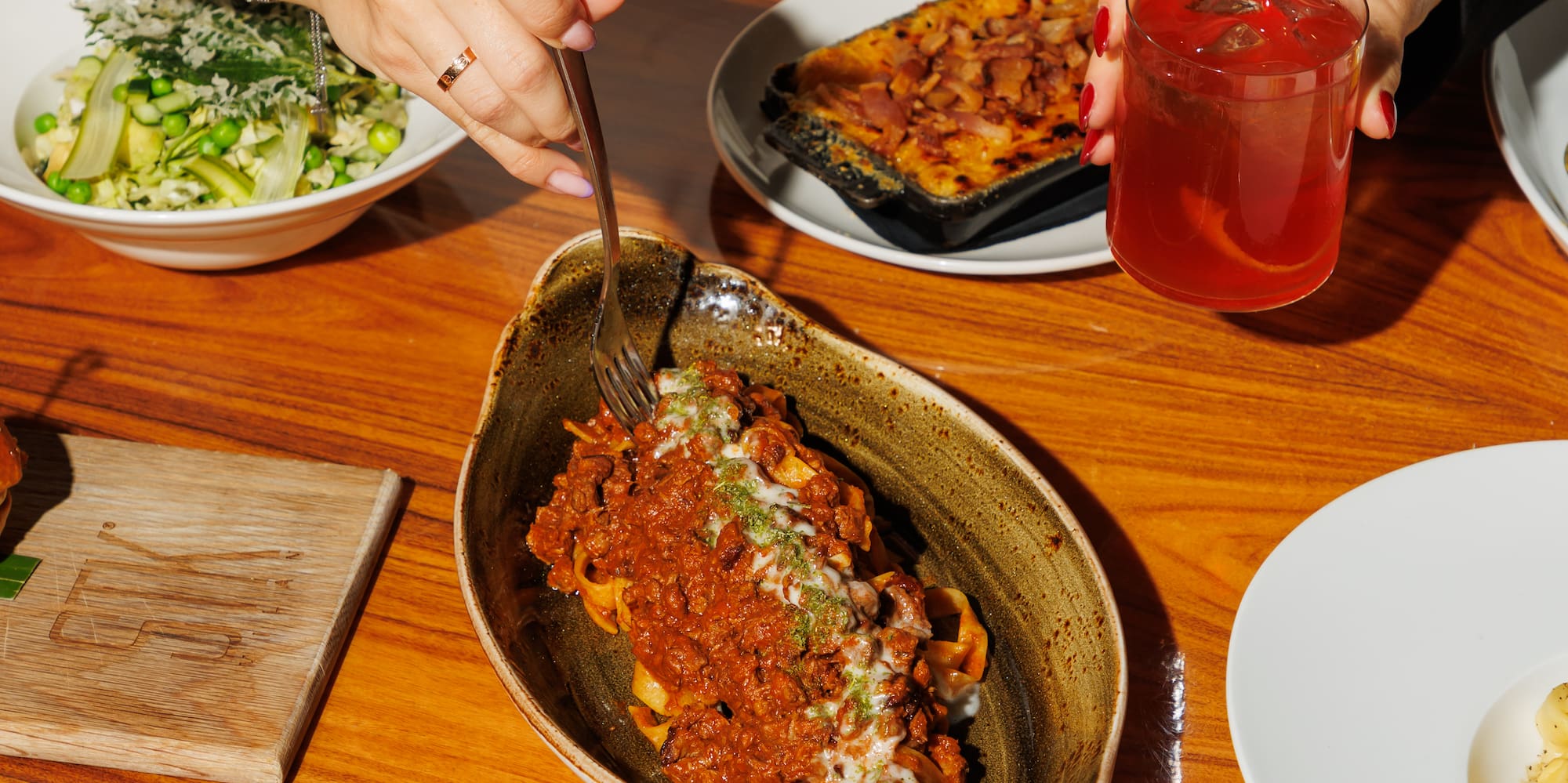 Table of Italian dishes: pasta bolognese, burrata, lamb chops, and cocktails.