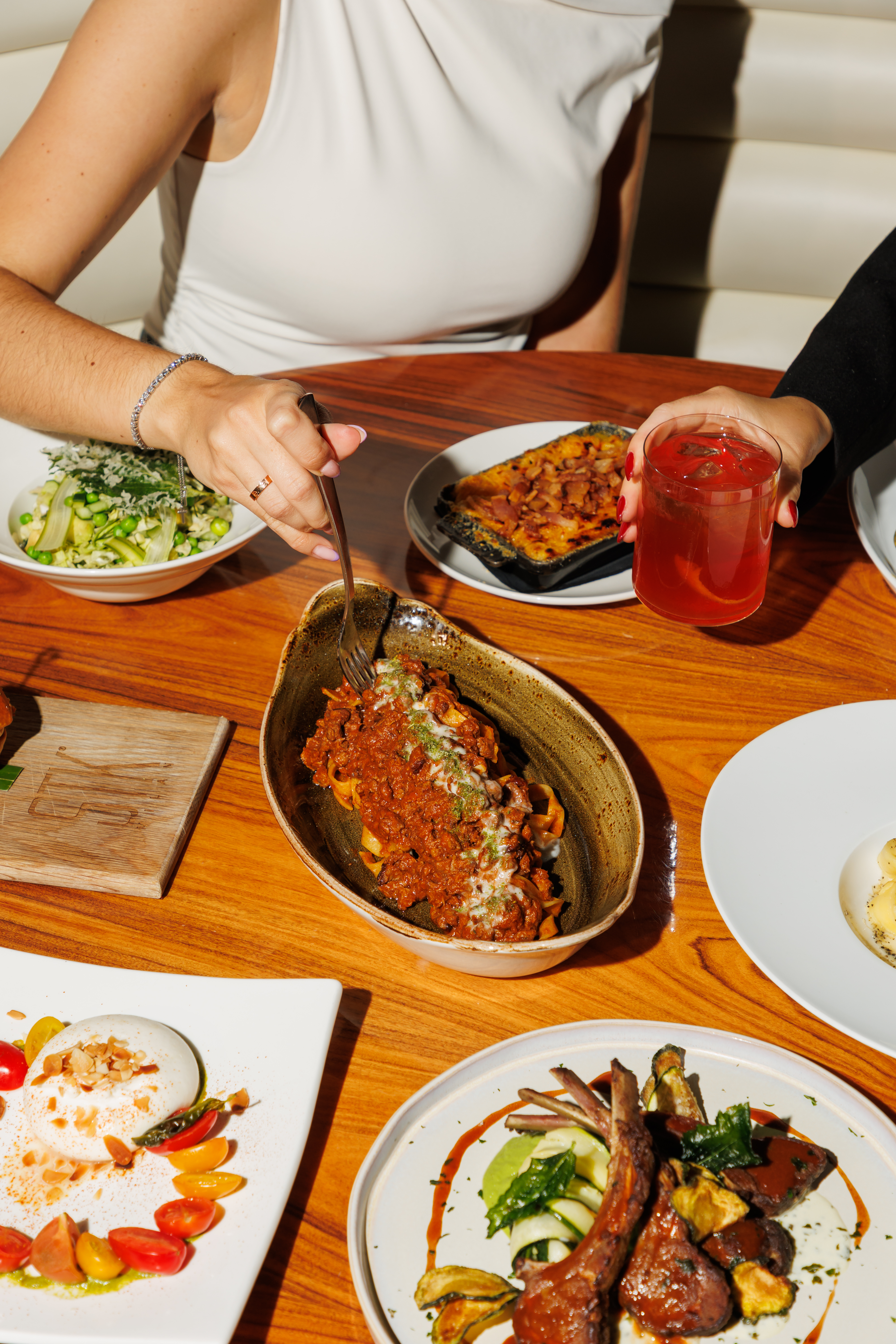 Table of Italian dishes: pasta bolognese, burrata, lamb chops, and cocktails.