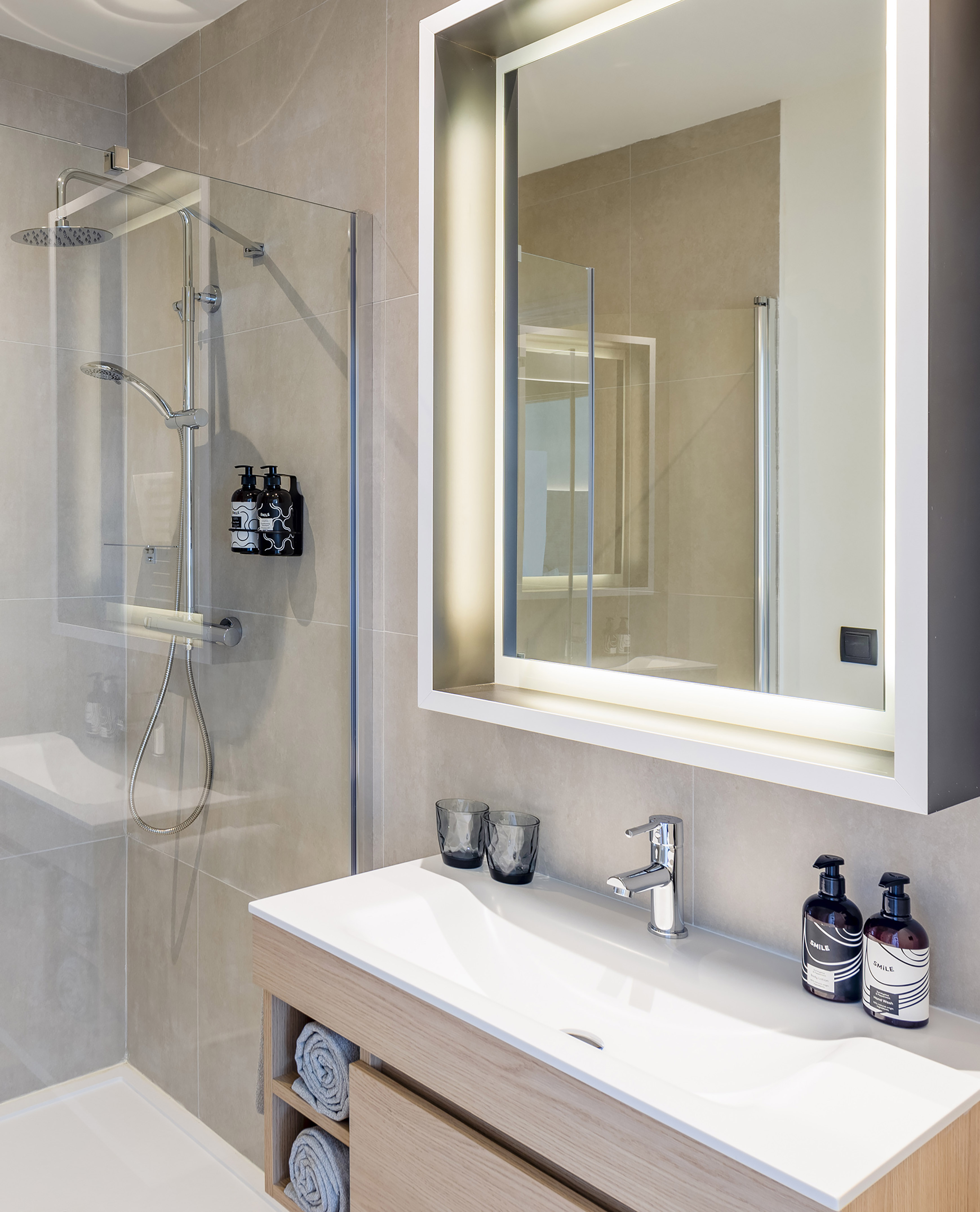 Modern hotel bathroom with walk-in shower, wooden vanity, and backlit mirror.