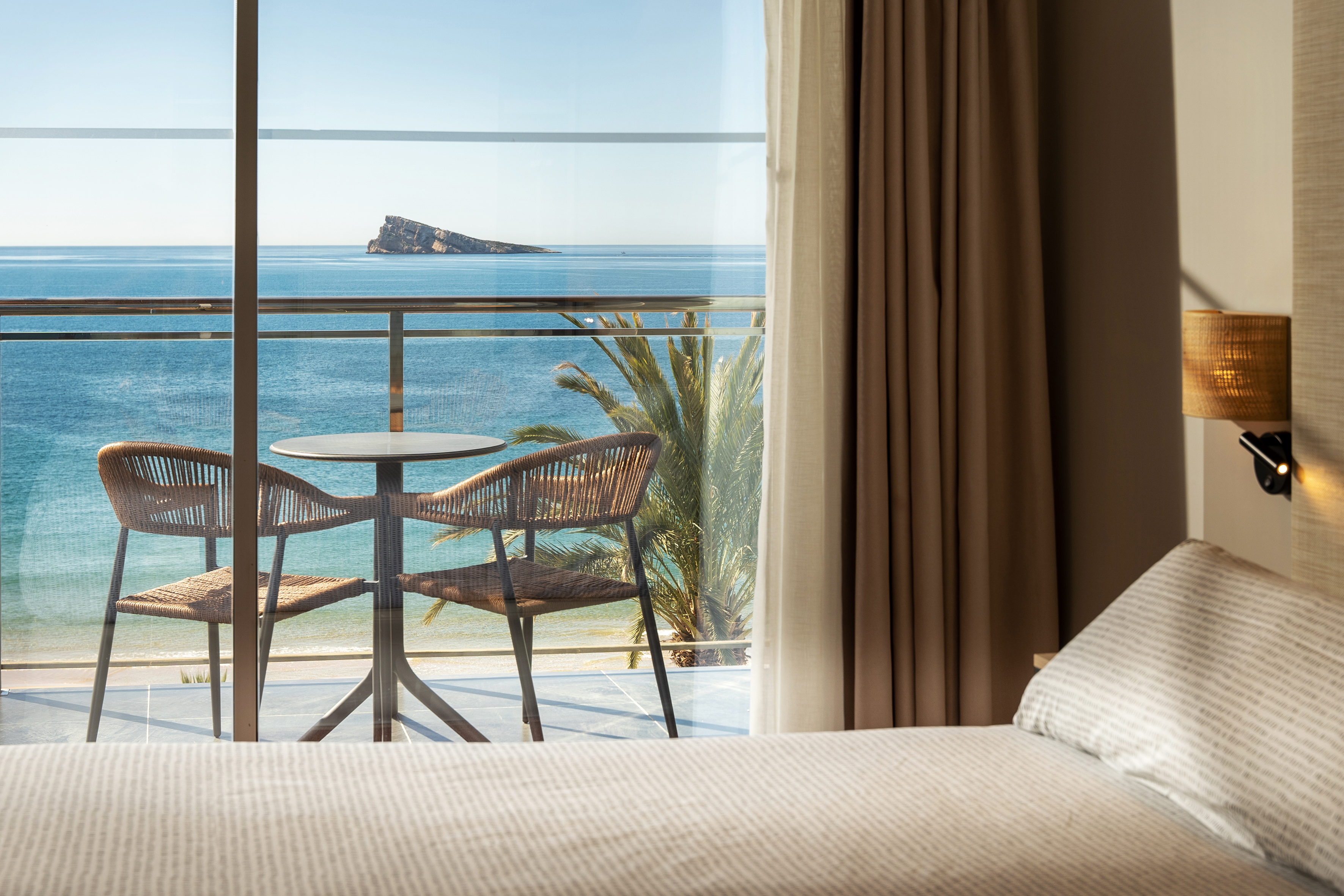 Hotel room balcony with wicker chairs, ocean view, distant island, and beach.