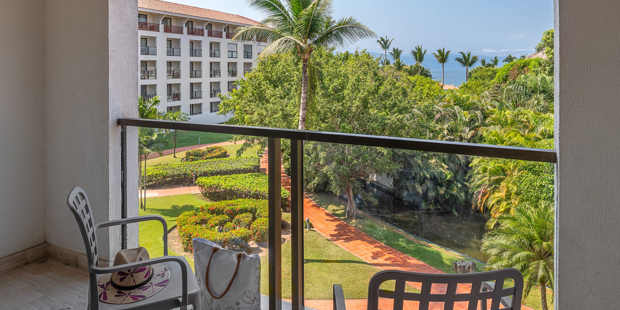 Hotel balcony with tropical garden, palm trees, and ocean view.