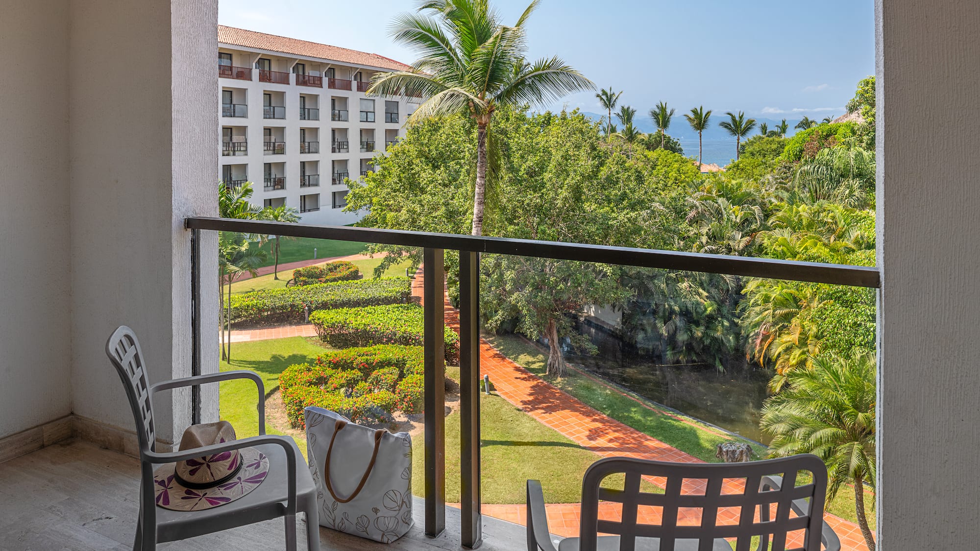 Hotel balcony with tropical garden, palm trees, and ocean view.