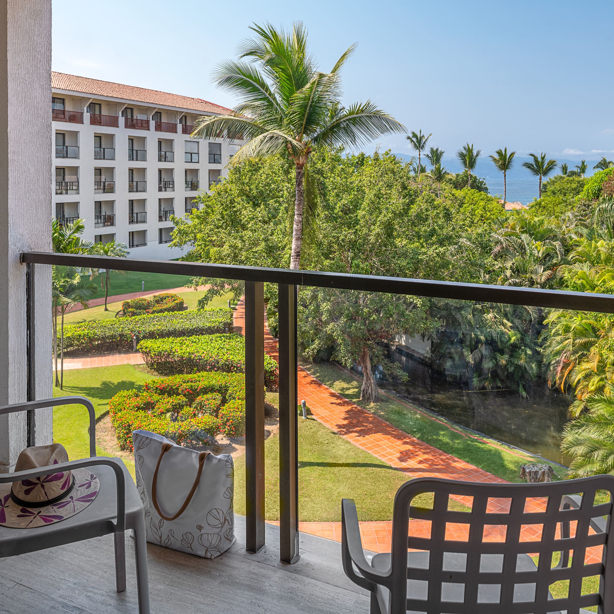 Hotel balcony with tropical garden, palm trees, and ocean view.