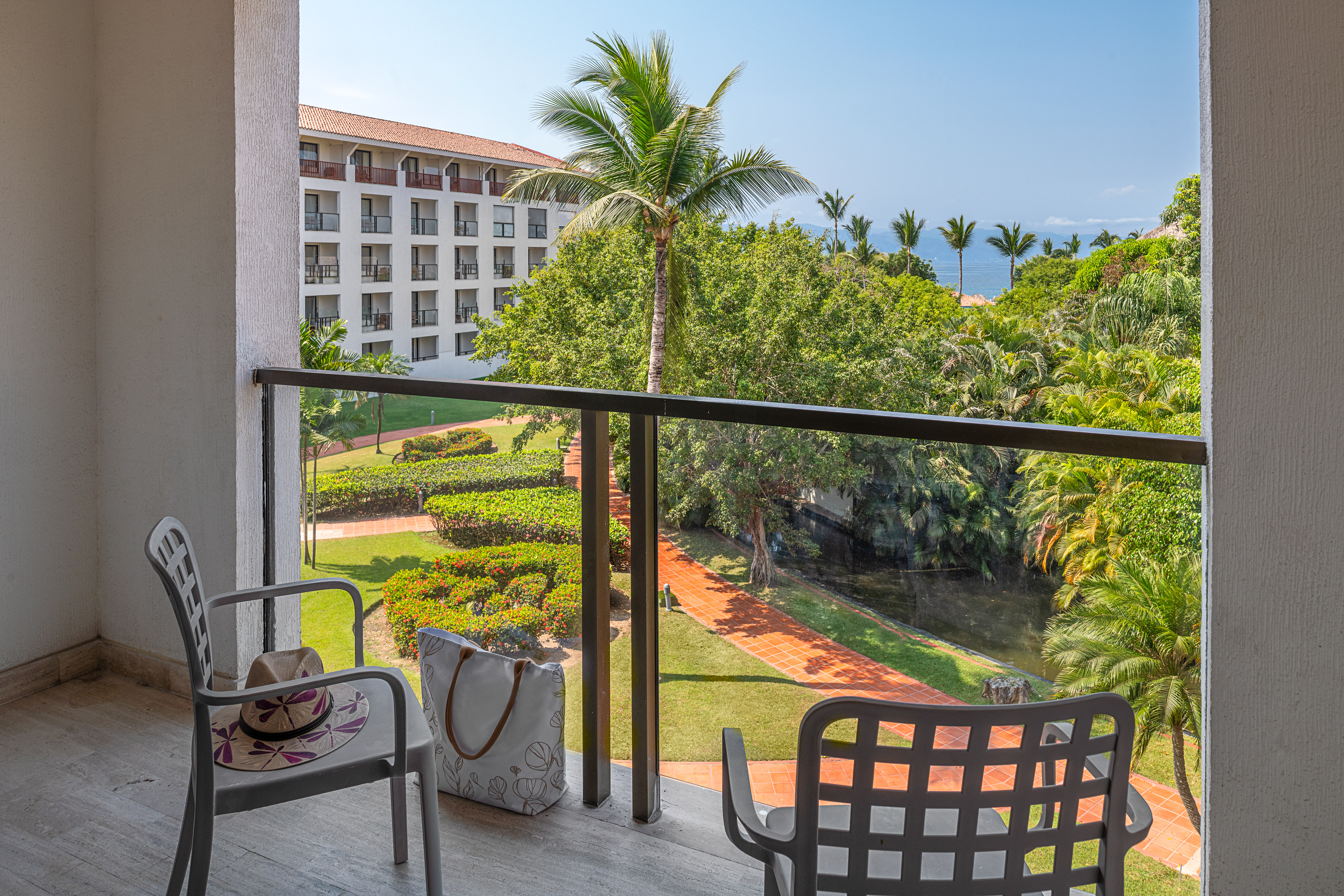 Hotel balcony with tropical garden, palm trees, and ocean view.