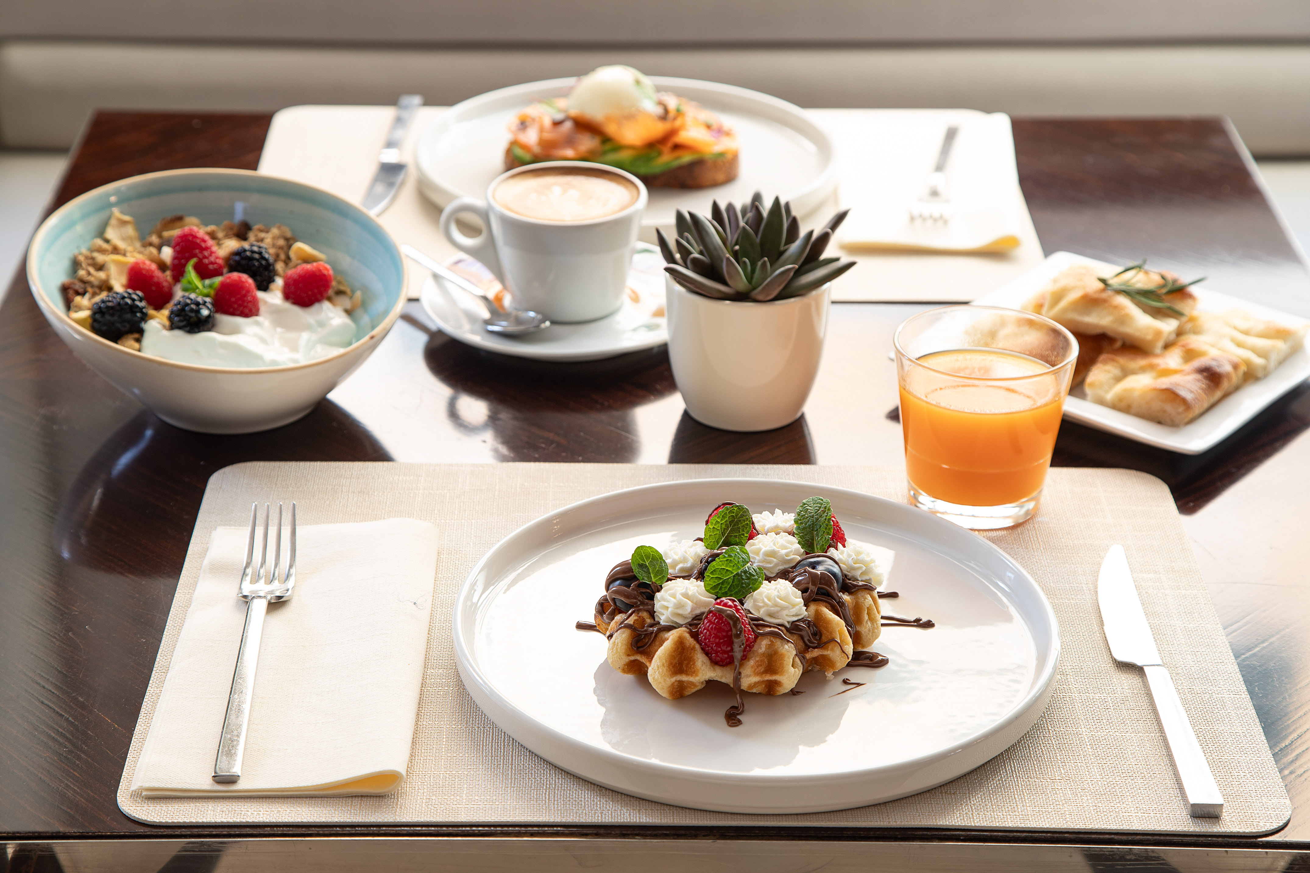 Breakfast spread with waffle, fruit yogurt, coffee, juice, and salmon toast.