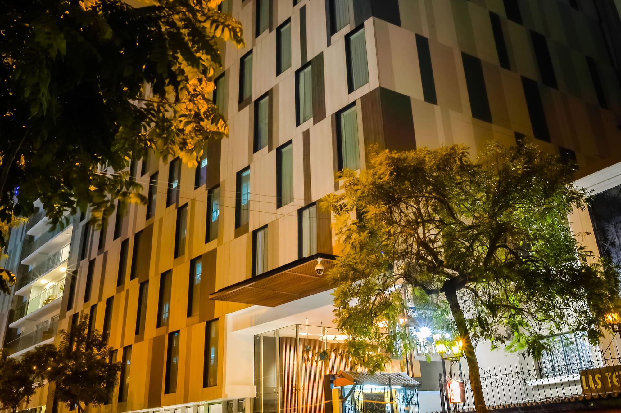 Illuminated modern hotel building at night, city street, trees, red light trails.